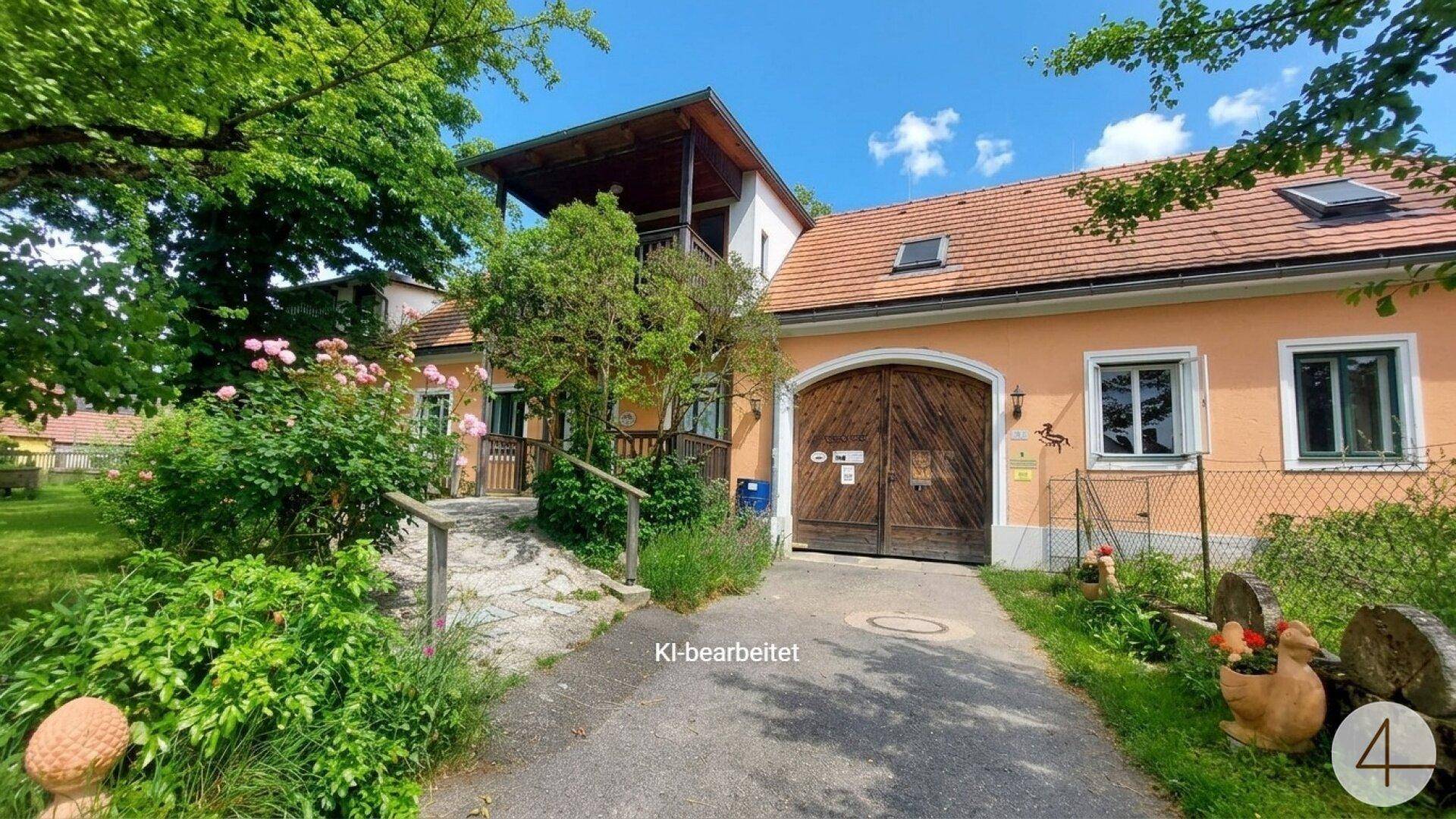 Ansicht des Landhauses mit großem Holztor, gepflasterter Auffahrt und blühenden Rosenbüschen im Vorgarten.