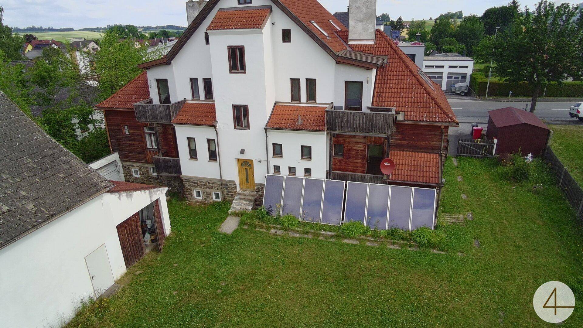 Rückseite des Gebäudes mit großem Rasen, Holzverkleidung, Balkonen und einer Photovoltaikanlage im Gartenbereich.