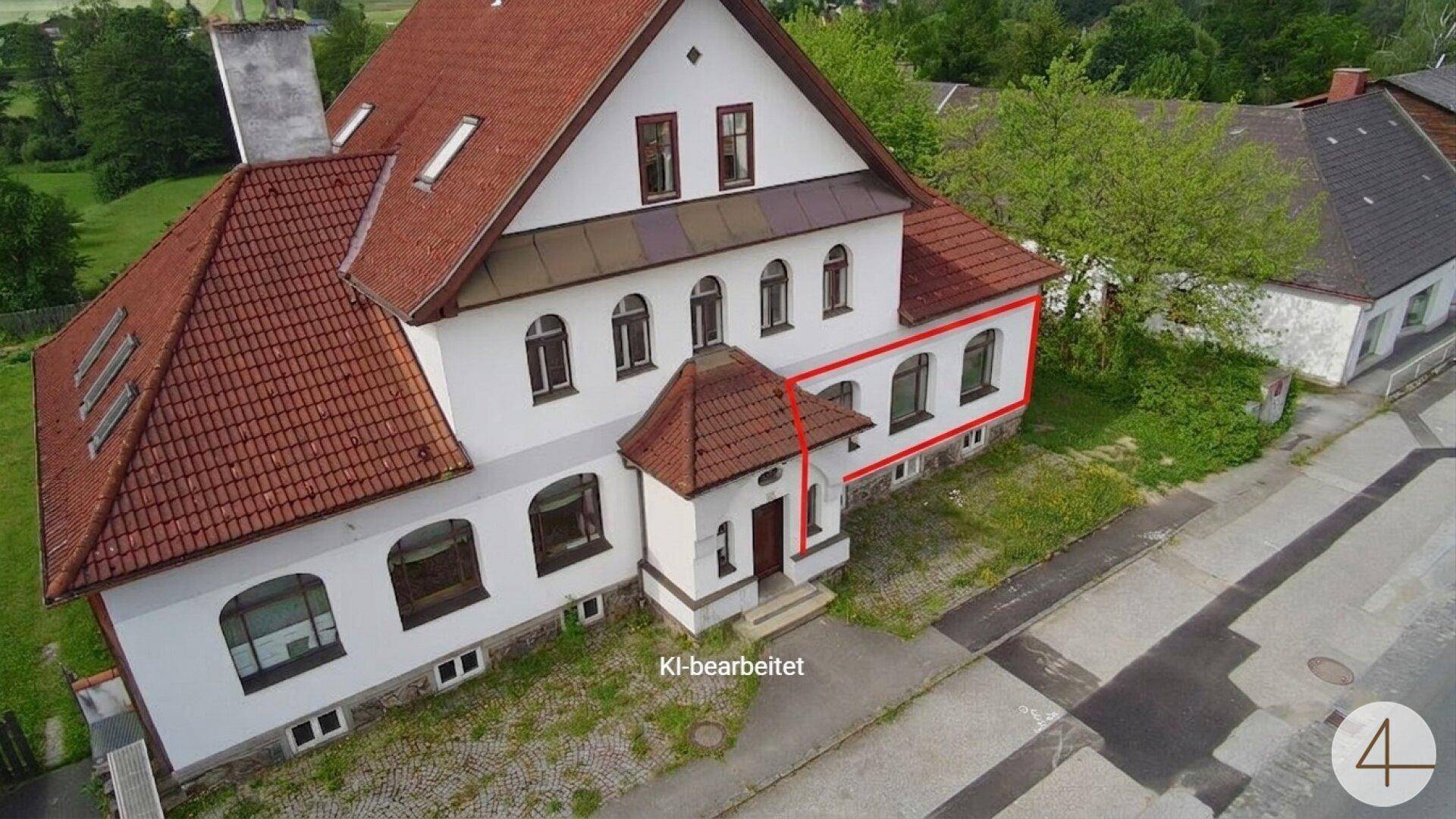 Historisches Gebäude mit weißer Fassade, rotem Ziegeldach und einem markanten Eingangsbereich, umgeben von Grünflächen.