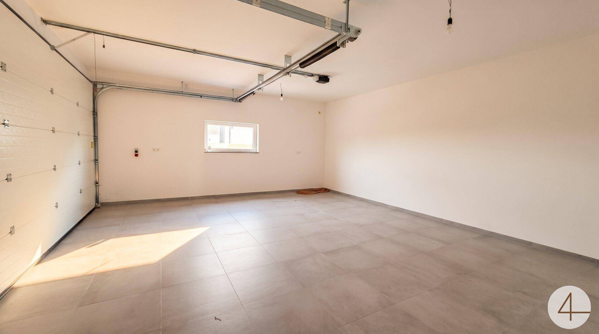 Geräumige, leere Garage mit Rolltor, Fliesenboden und einem Fenster für Tageslicht.