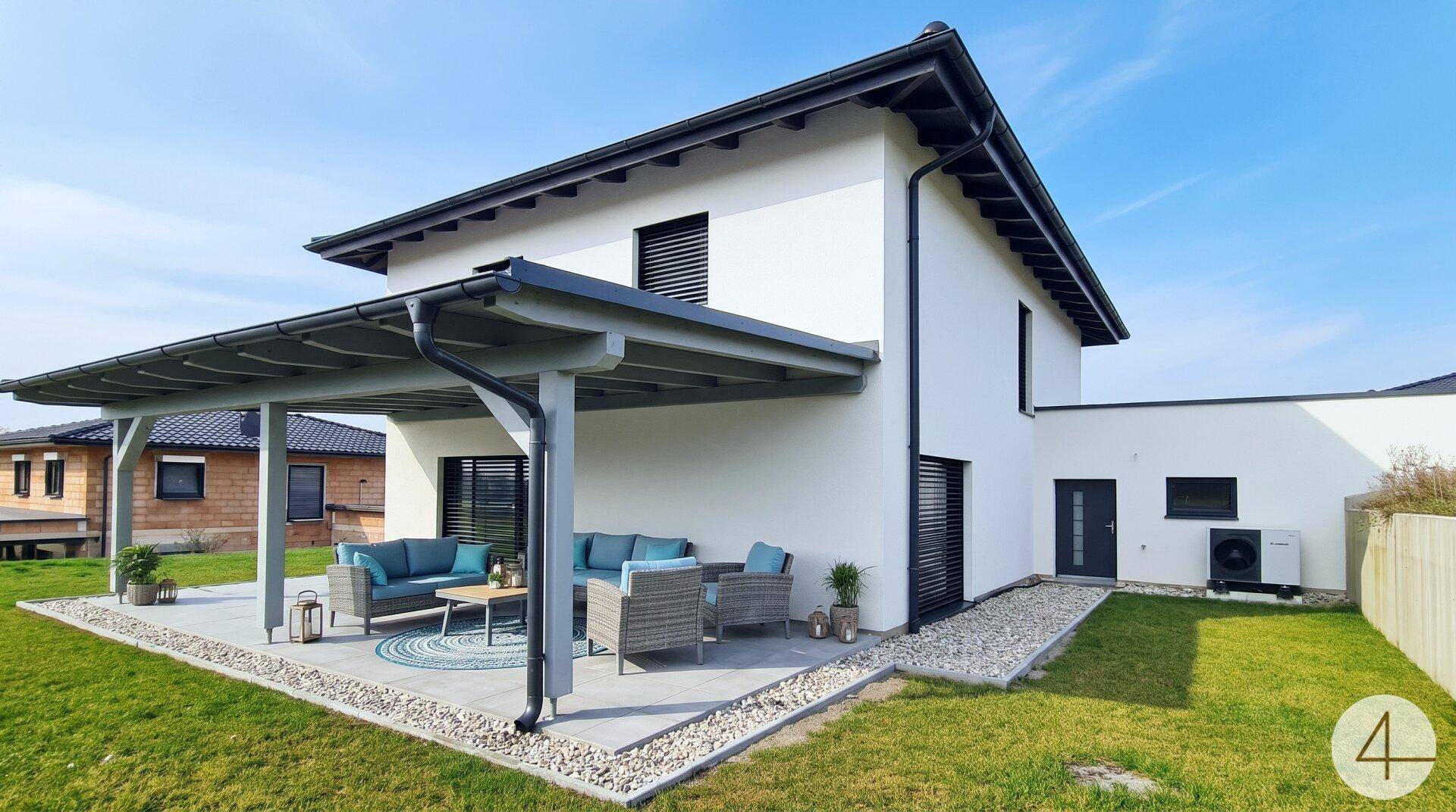 Überdachte Terrasse mit bequemen Gartenmöbeln und angrenzender Rasenfläche am Neubau.