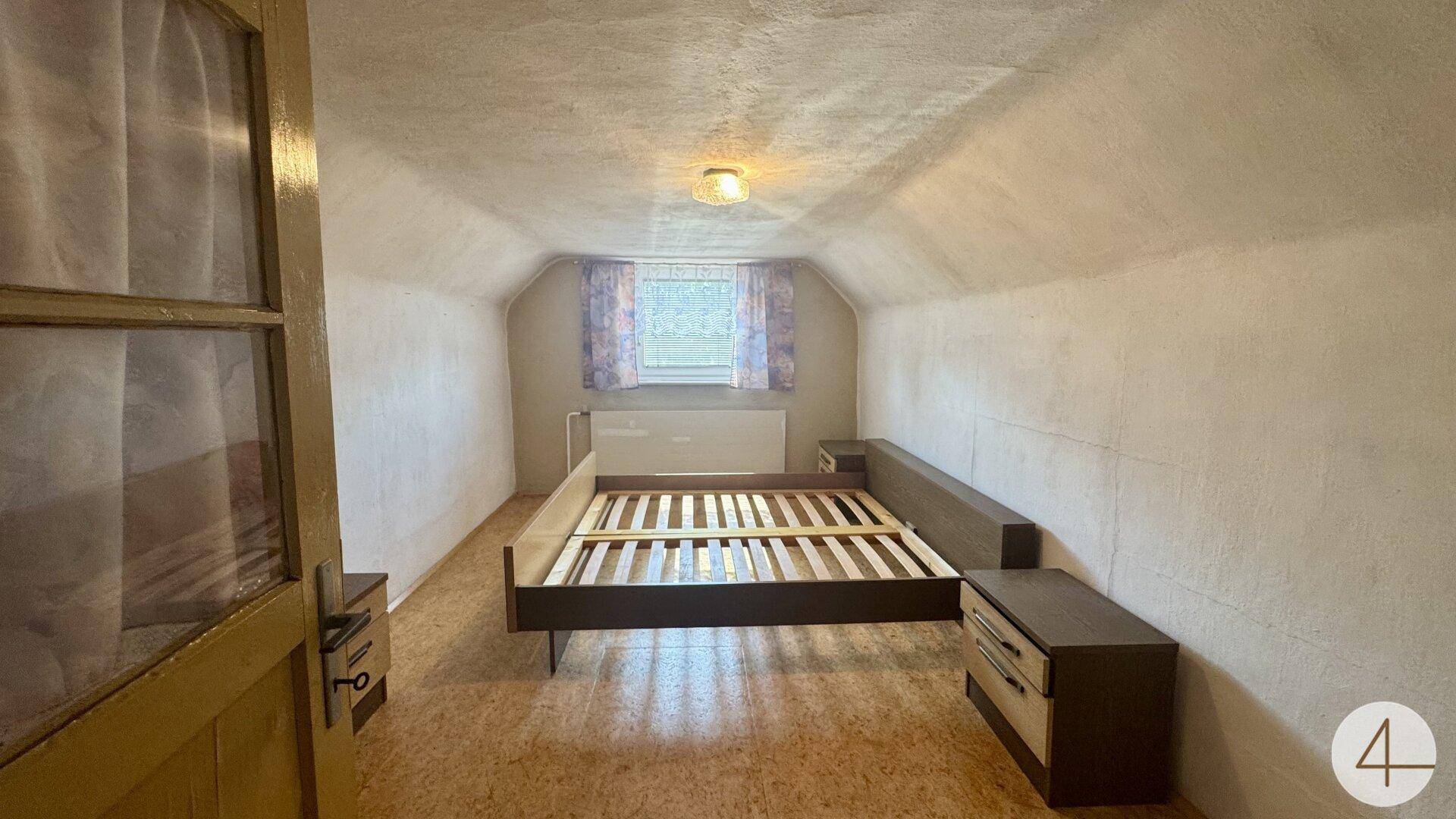 Dachgeschoss-Schlafzimmer mit schrägen Wänden, Bettrahmen und einem Fenster.