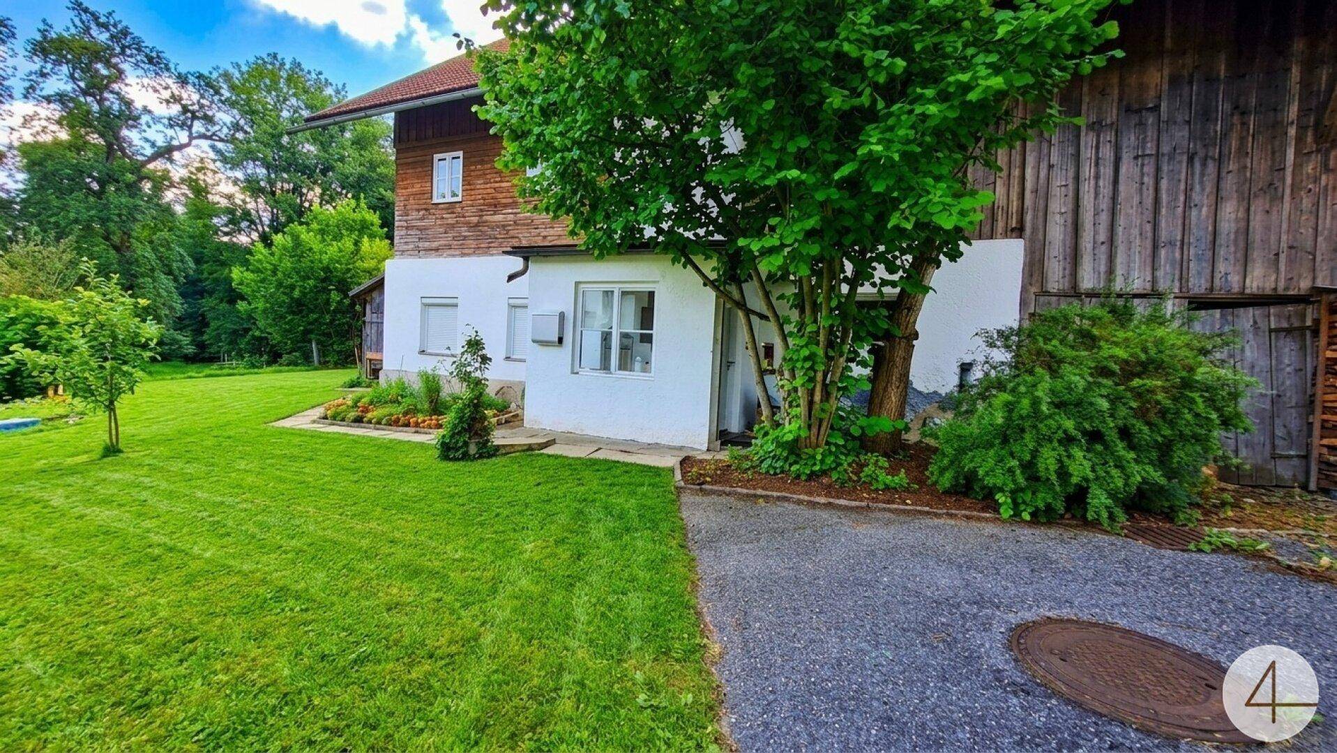 Seitenansicht des Hauses mit gepflegtem Rasen, Blumenbeeten und einer asphaltierten Zufahrt.