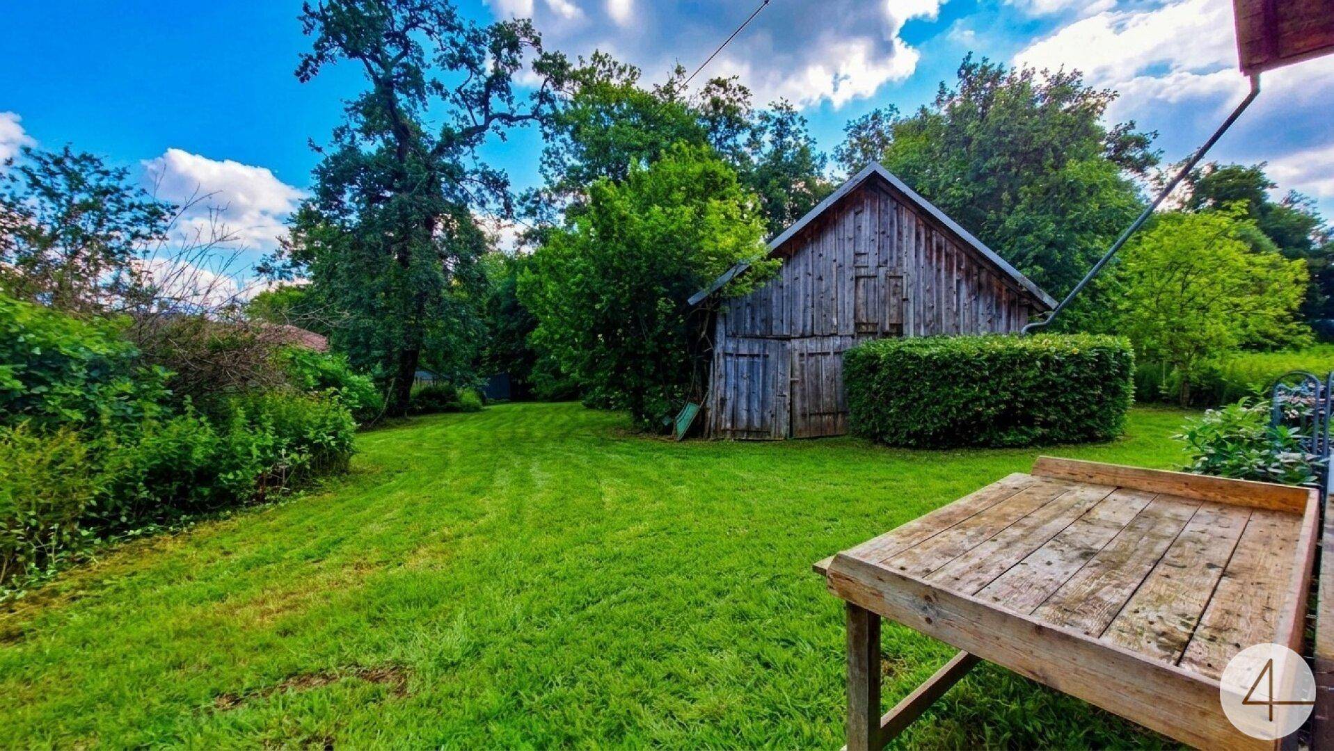 Rustikales Holzgebäude im weitläufigen grünen Garten mit gepflegtem Rasen und Hecken.
