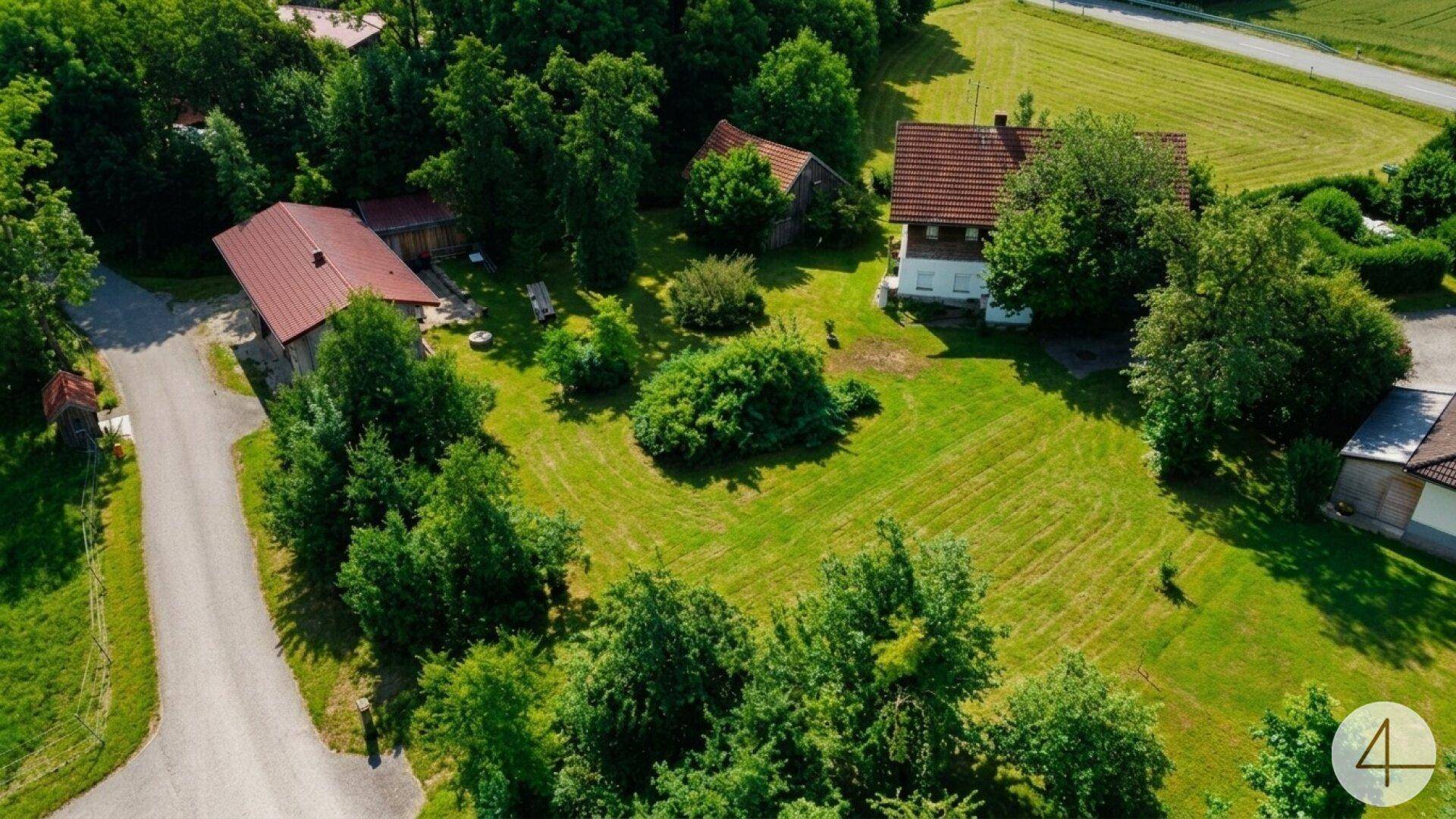 Luftaufnahme eines ländlichen Anwesens mit mehreren Gebäuden, umgeben von weiten Grünflächen und Bäumen.