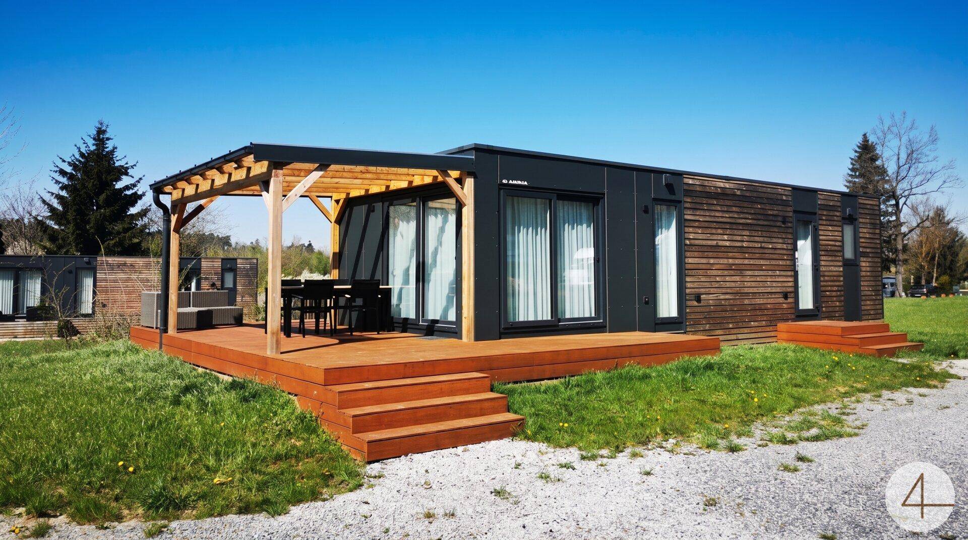 Modernes Modulhaus mit Holzfassade und großer Holzterrasse unter einer Pergola.