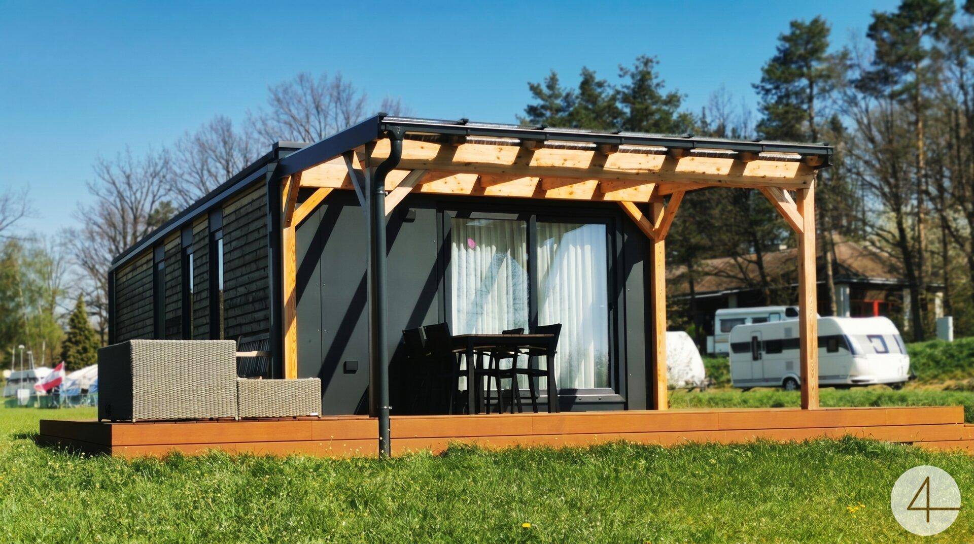 Vorderansicht des Modulhauses mit Holzterrasse, Pergola und gemütlichen Outdoor-Möbeln.