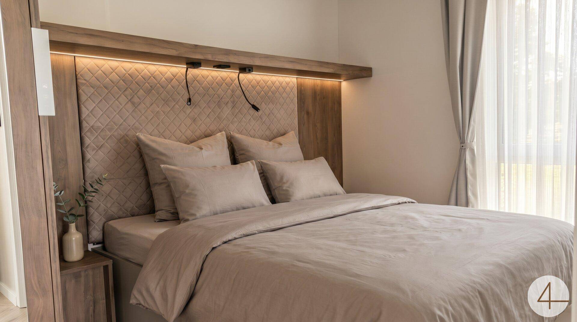 Gemütliches Schlafzimmer mit Doppelbett, gepolstertem Kopfteil und integrierter Beleuchtung.
