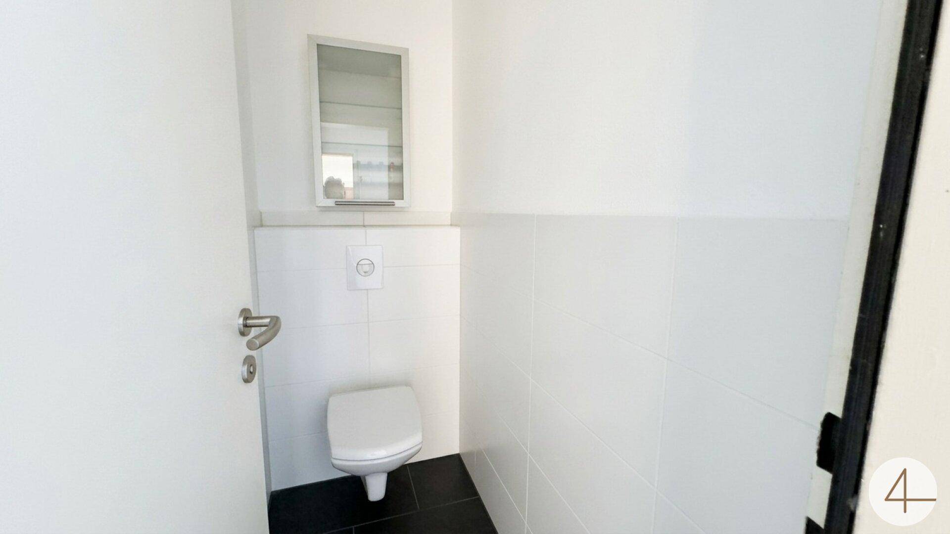 Kleines Gäste-WC mit weißen Fliesen, schwarzem Boden und wandhängendem WC.