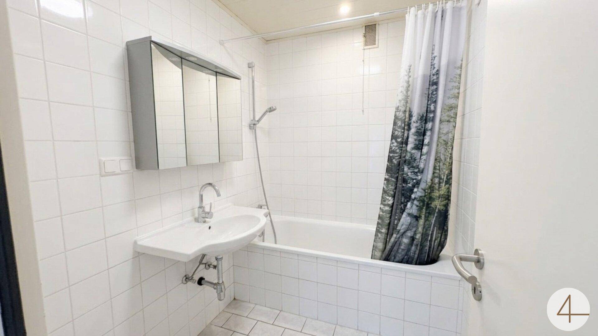 Helles Badezimmer mit Badewanne, Duschvorhang, Waschbecken und Spiegelschrank.