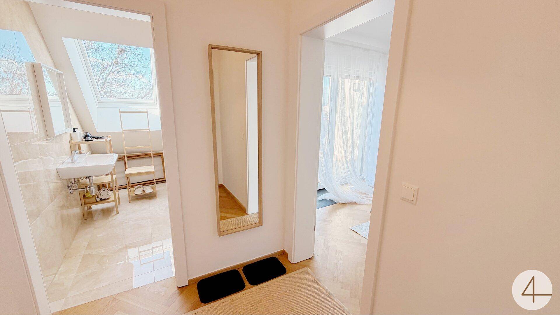 Heller Flur mit Spiegel und Zugang zu einem modernen Badezimmer mit Dachfenster und einem weiteren Zimmer.