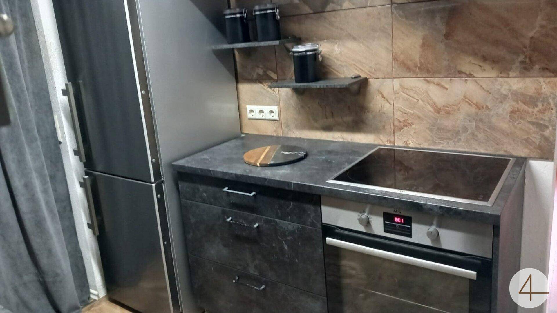 Funktional ausgestattete Küche mit Einbaukühlschrank, Backofen und dunklen Schränken.