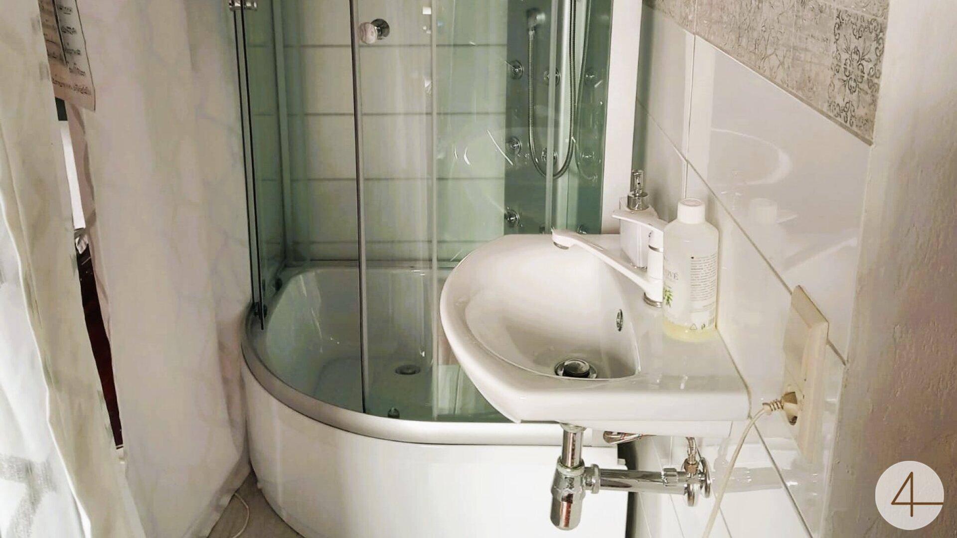 Kleines Badezimmer mit Eckduschkabine, wandmontiertem Waschbecken und weißen Fliesen.