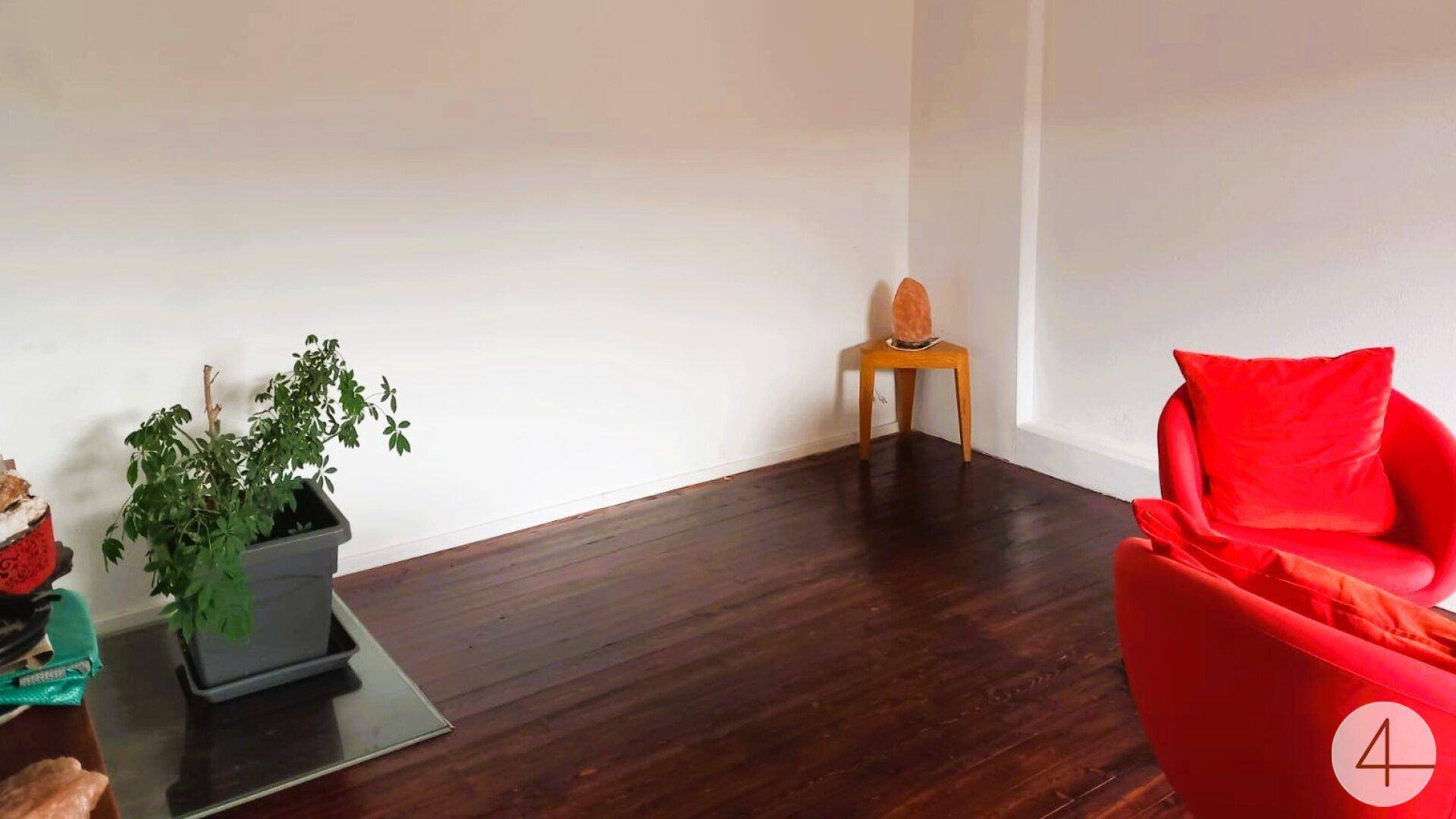 Helles Wohnzimmer mit dunklem Holzboden, weißen Wänden und einem roten Sessel als Farbakzent.