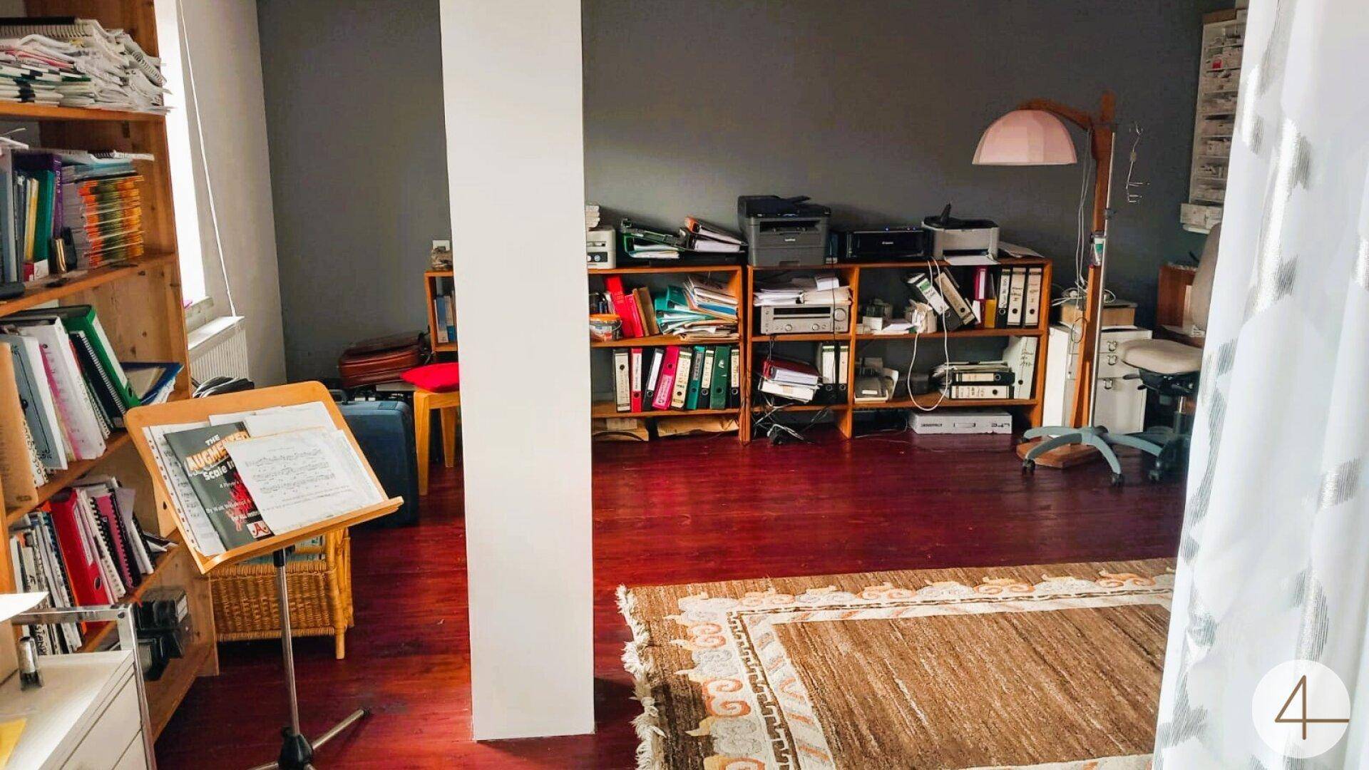 Arbeitszimmer mit zahlreichen Bücherregalen, dunklem Holzboden und einem Teppich.