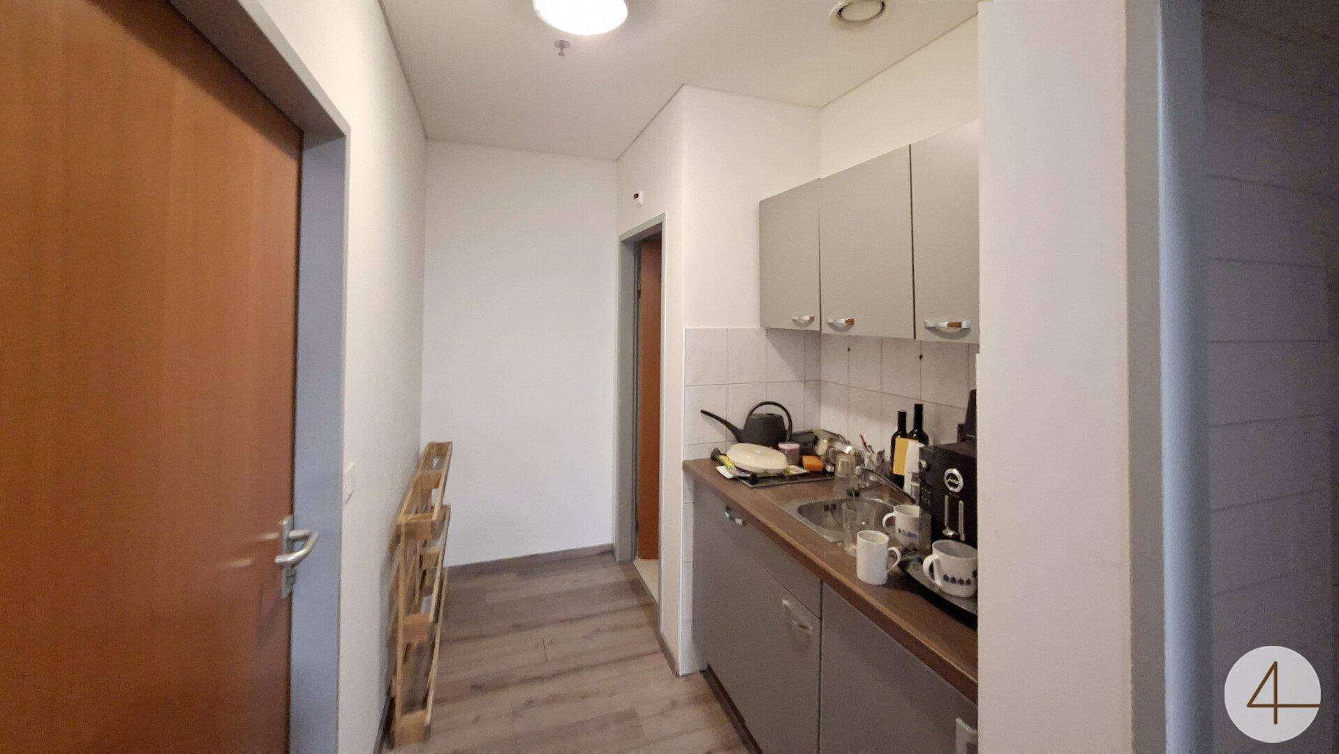 Kleine Küchenzeile mit grauen Schränken, Spüle und einer Kaffeemaschine, ideal für kurze Pausen.