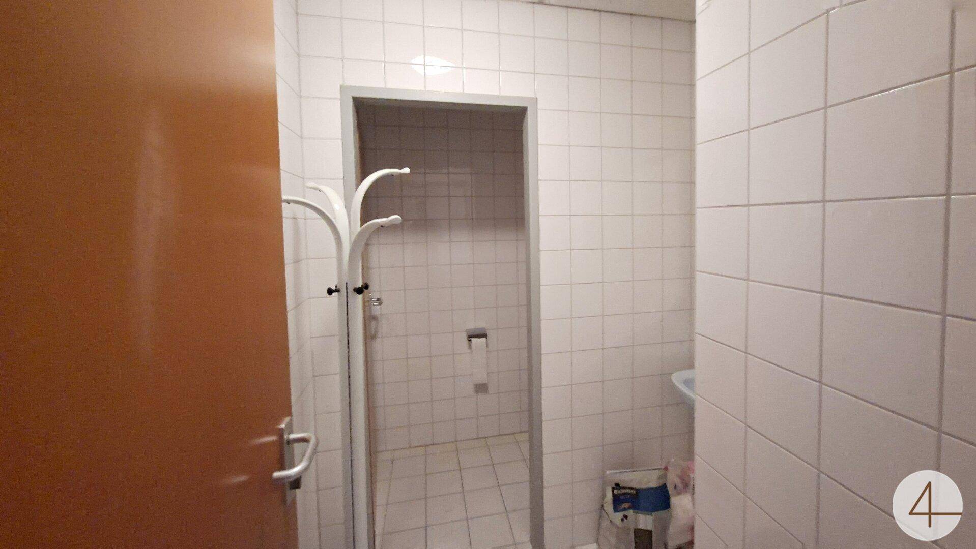 Badezimmer oder Toilette, komplett gefliest in Weiß, mit einer Garderobe und einfacher Ausstattung.