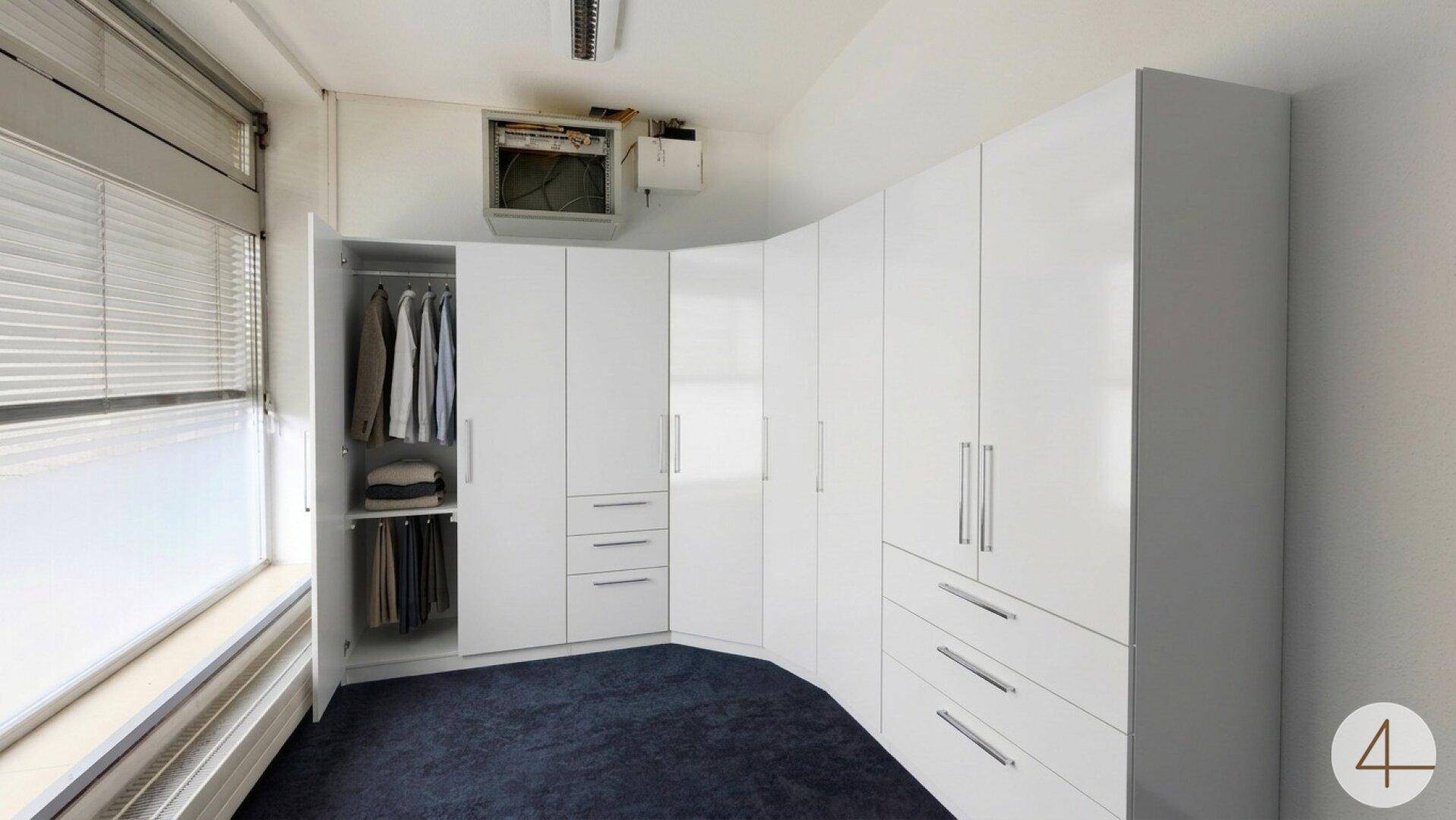Heller Raum mit weißen Einbauschränken und Fenster mit Jalousien, ideal als Ankleidezimmer.