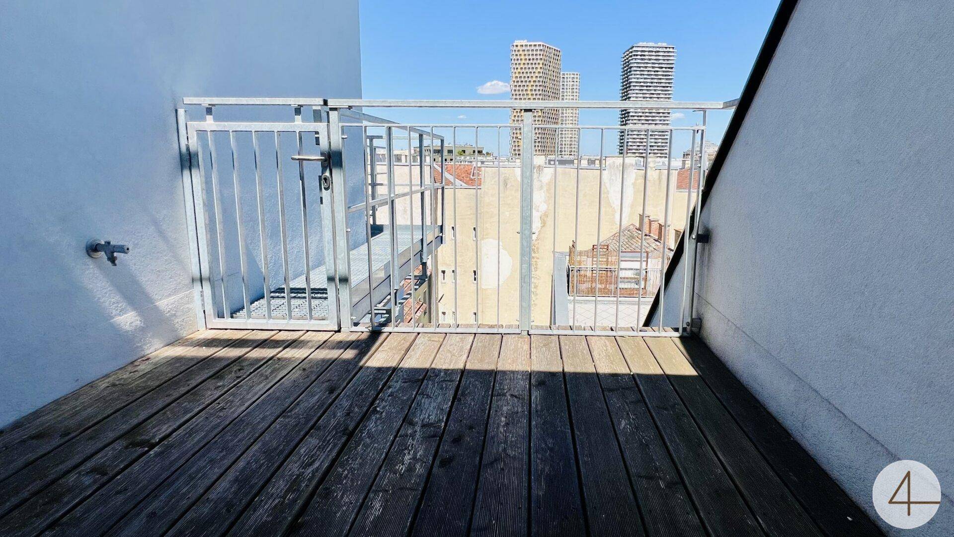 Kleiner Balkon mit Holzboden und Metallgeländer, bietet einen Blick auf die Stadt und Hochhäuser.