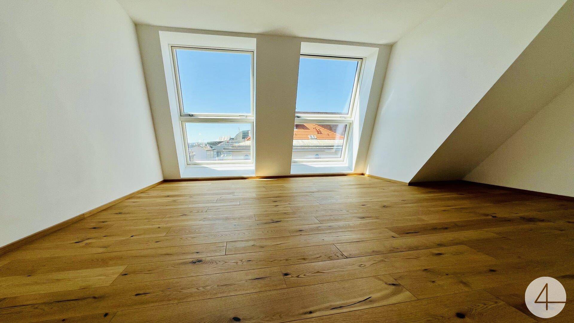Heller Raum im Dachgeschoss mit Holzboden und zwei großen Dachfenstern, die viel Licht spenden.