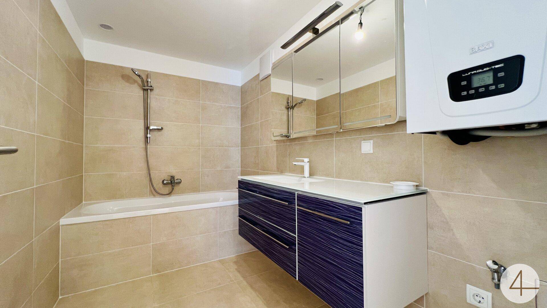 Modernes Badezimmer mit beigefarbenen Fliesen, Badewanne mit Duschfunktion und stilvollem Waschtisch.