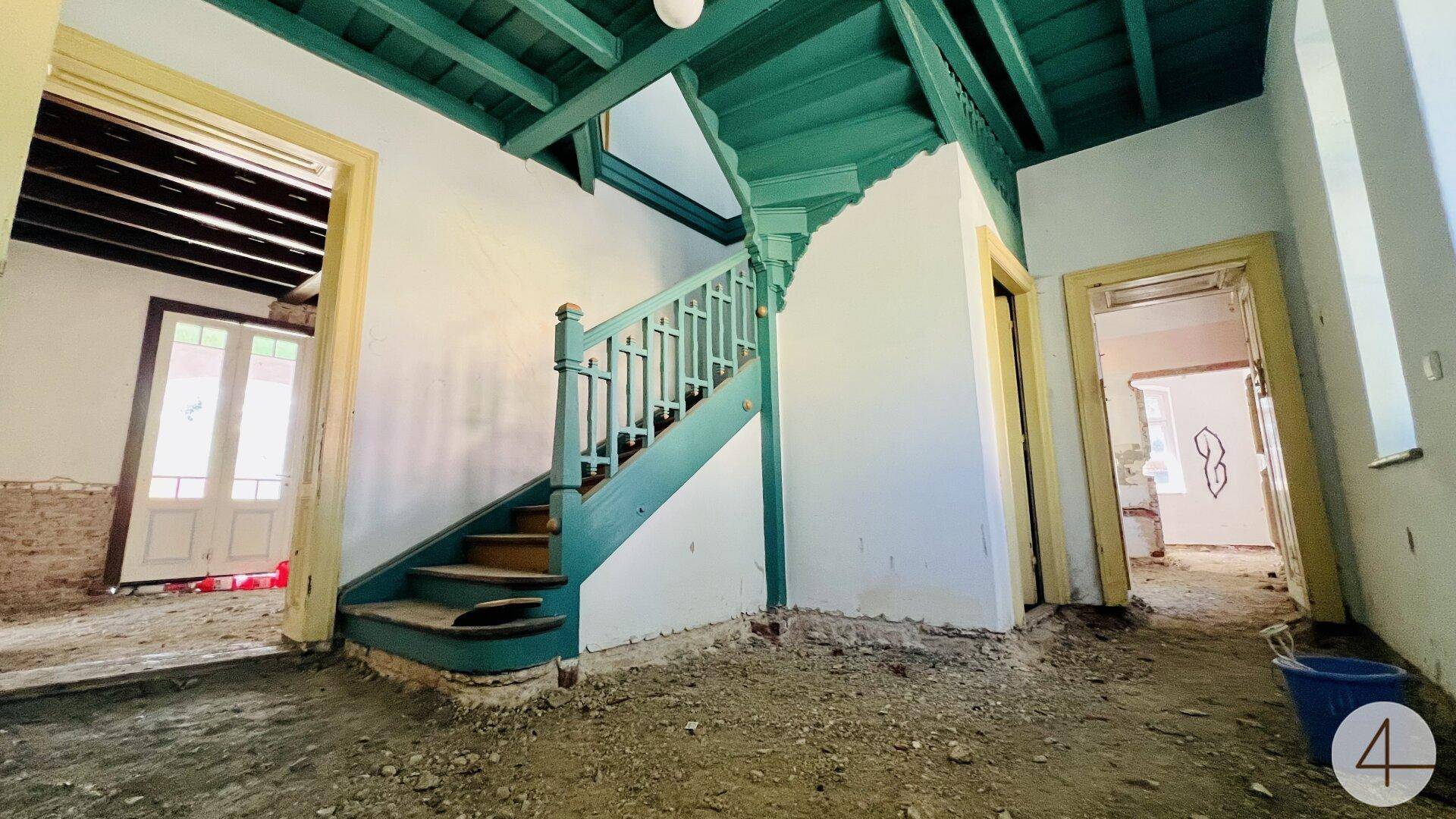 Alter Treppenaufgang mit grünen Holzgeländern und sichtbaren Deckenbalken in einem renovierungsbedürftigen Zustand.
