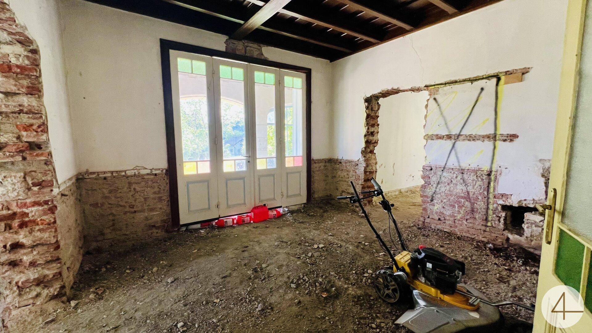 Renovierungsbedürftiger Raum mit freigelegten Ziegelwänden und alten Flügeltüren mit Buntglas.