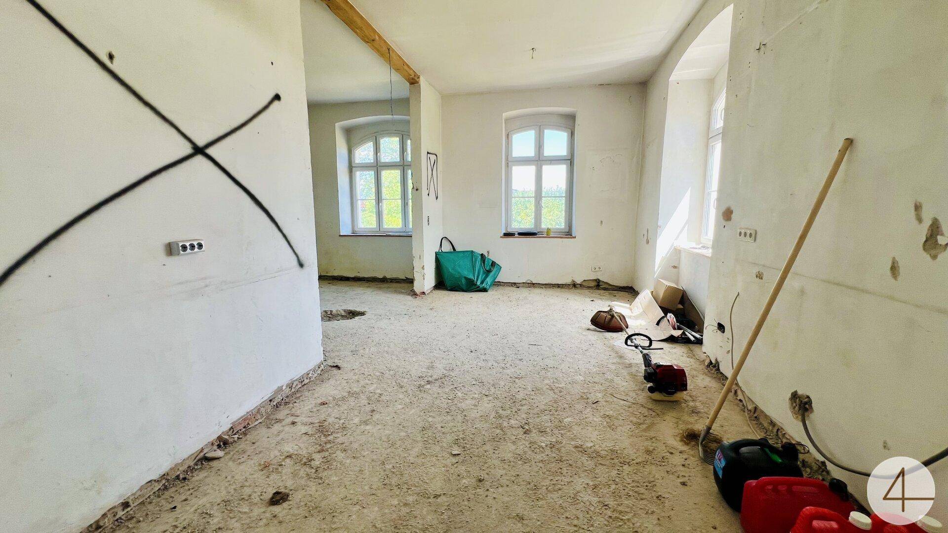 Großer, heller Raum in Renovierung mit zwei Fenstern und unfertigem Boden, bereit für den Ausbau.