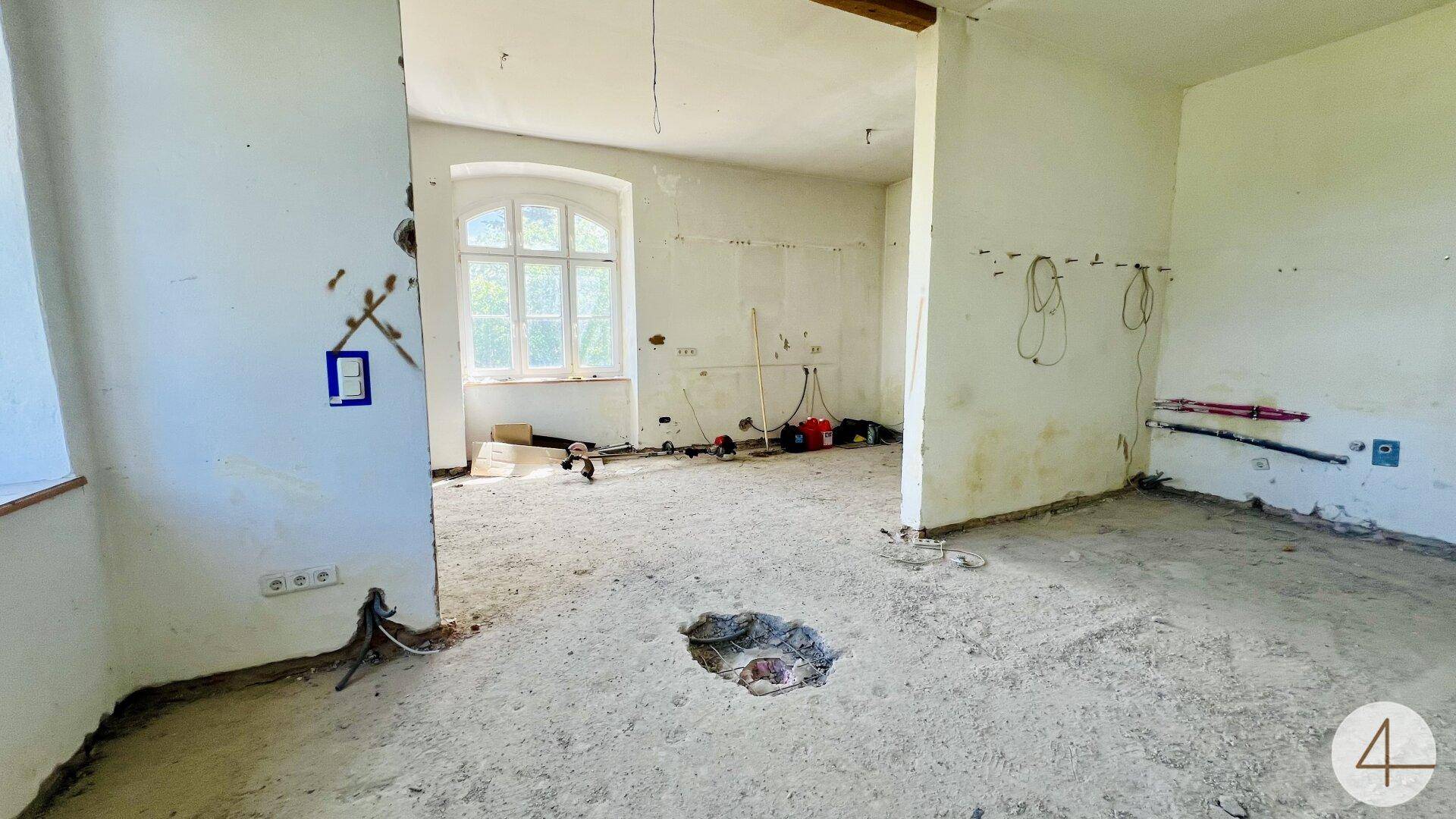 Renovierungsbedürftiger Raum mit sichtbaren Installationen und einem Fenster, bereit für den weiteren Ausbau.