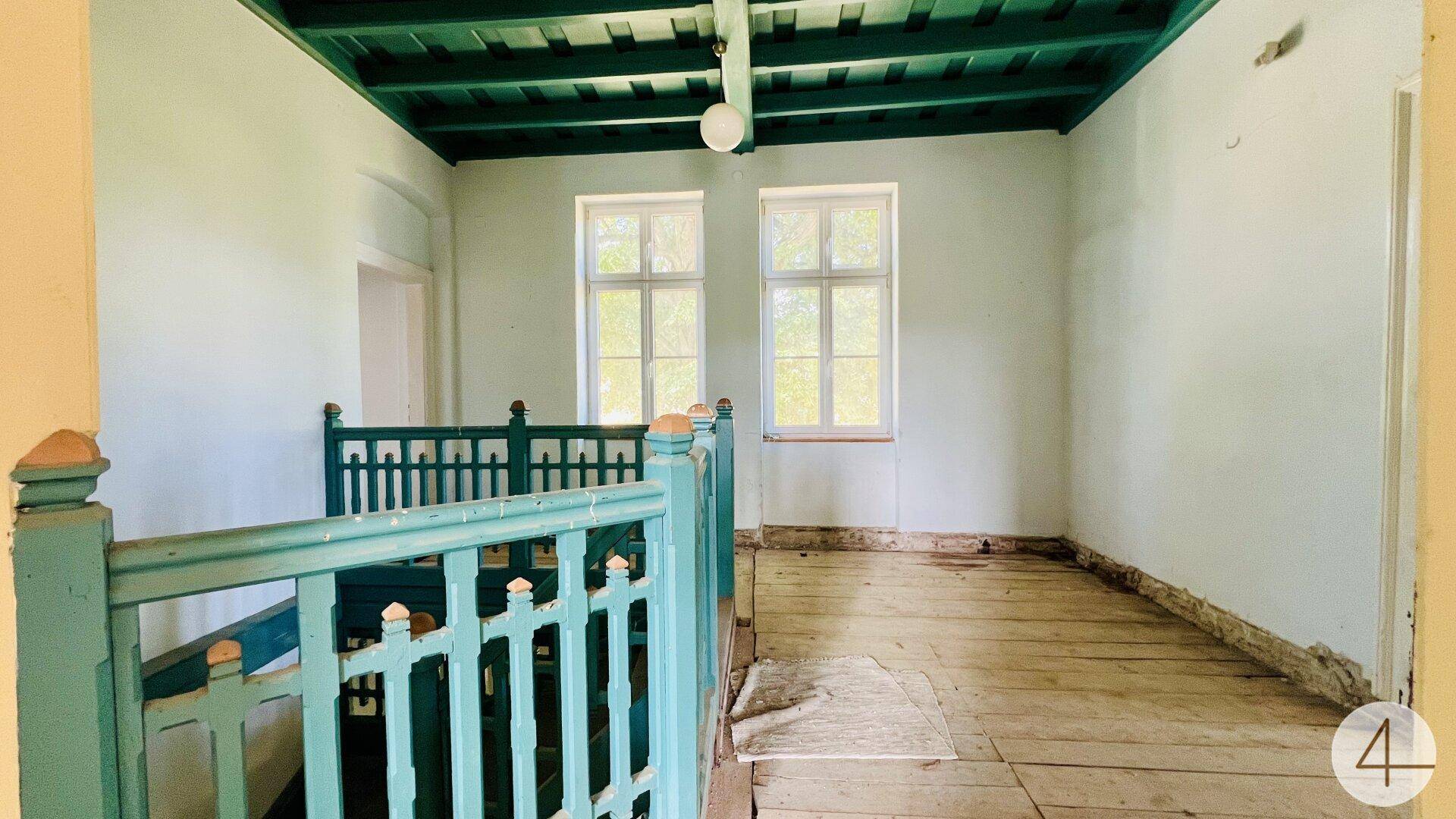 Heller Treppenabsatz mit Holzdielenboden, zwei Fenstern und einer auffälligen grünen Balkendecke.