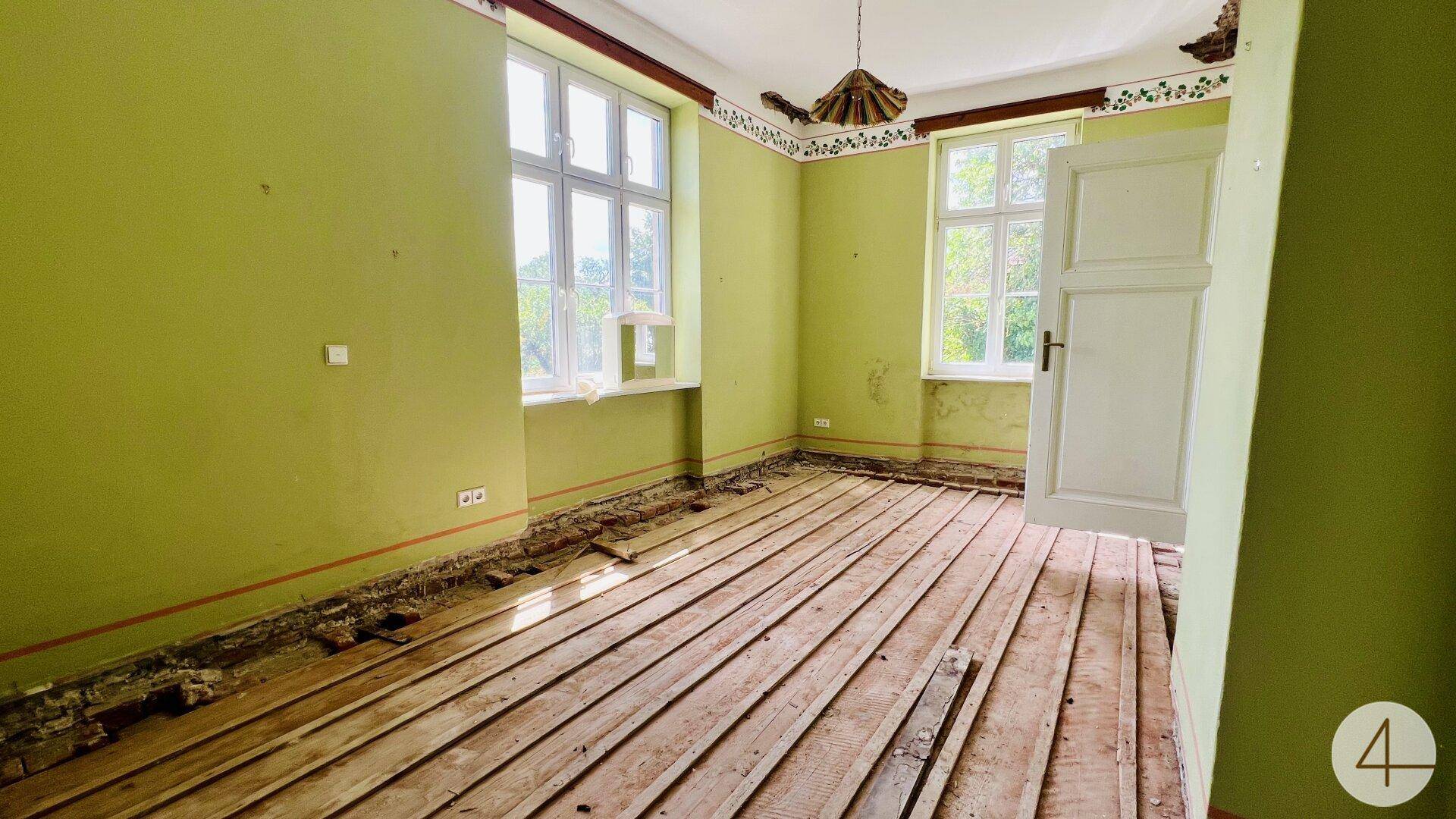 Zimmer mit grünen Wänden, freigelegten Holzdielen und dekorativen Elementen an der Decke, in Renovierung.