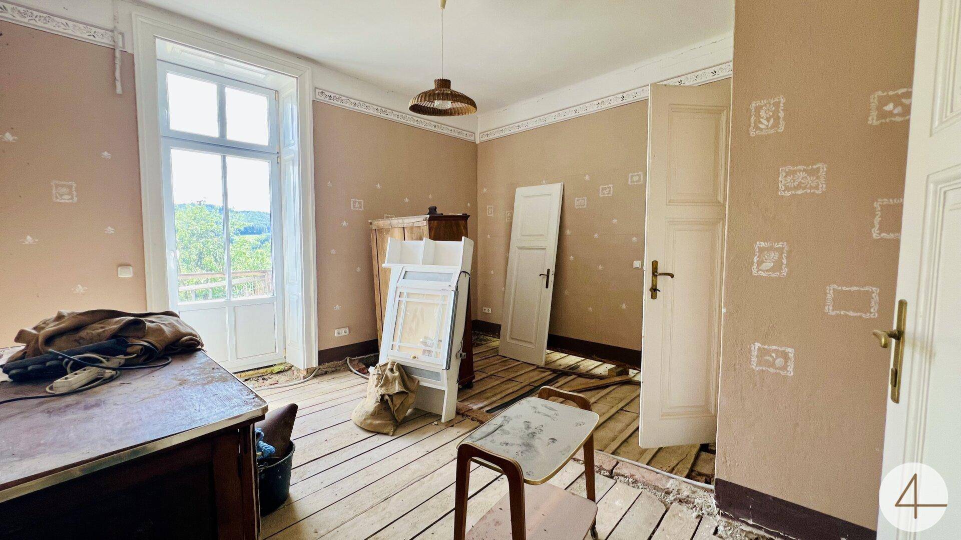 Geräumiges Zimmer mit hellbraunen Wänden, Holzdielenboden und Zugang zu einem Außenbereich, in Renovierung.
