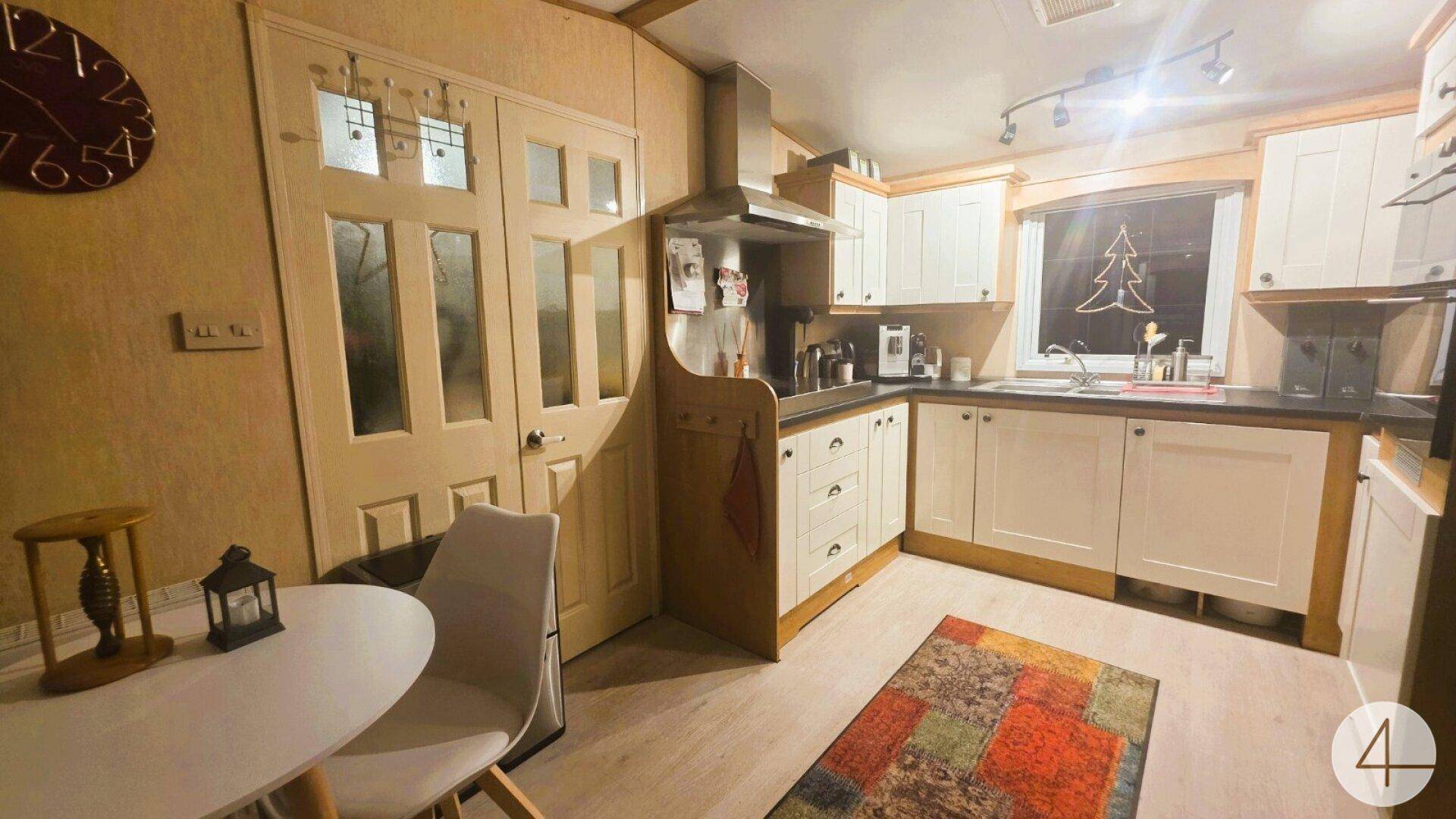 Funktionale Küche mit hellen Schränken, Essbereich und einem bunten Teppich auf dem Laminatboden.
