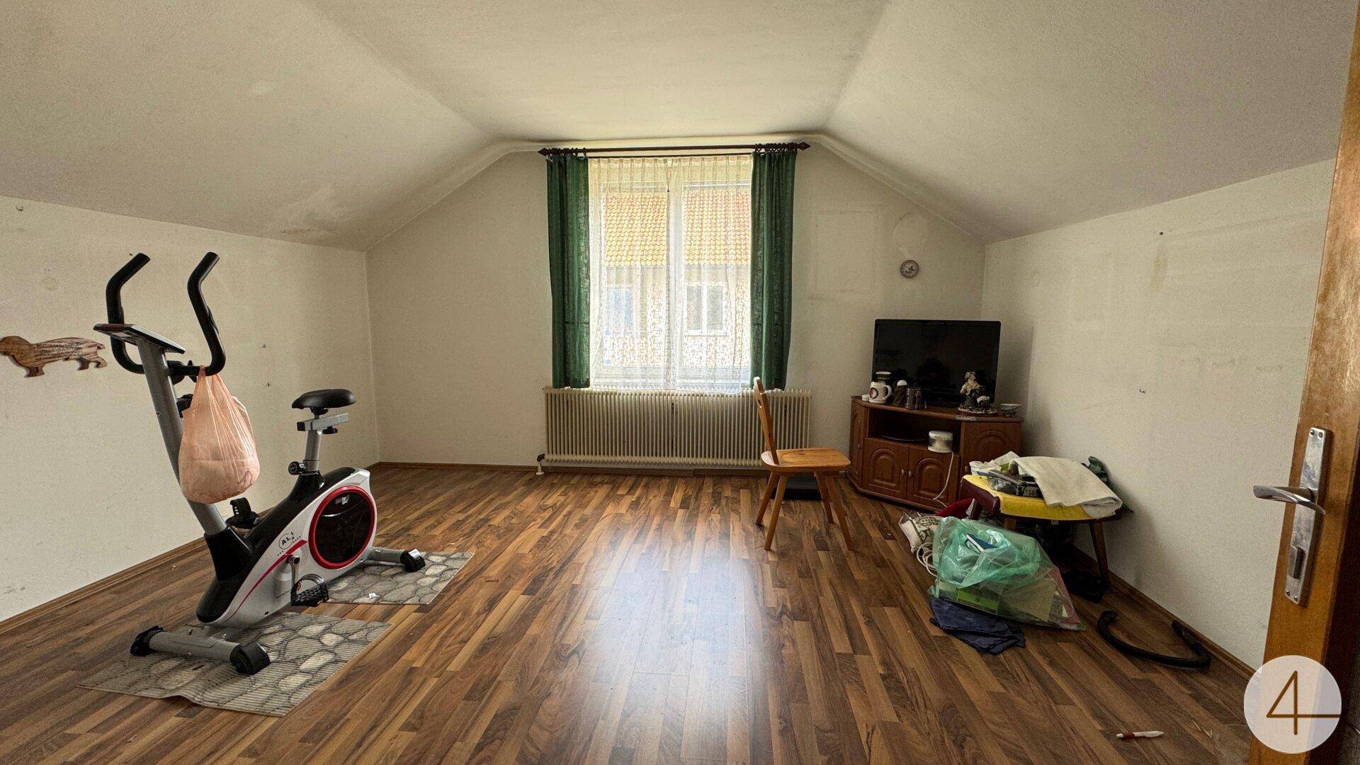 Vielseitiger Raum im Dachgeschoss mit Schrägdach, Laminatboden und Fenster, derzeit als Fitnessraum genutzt.