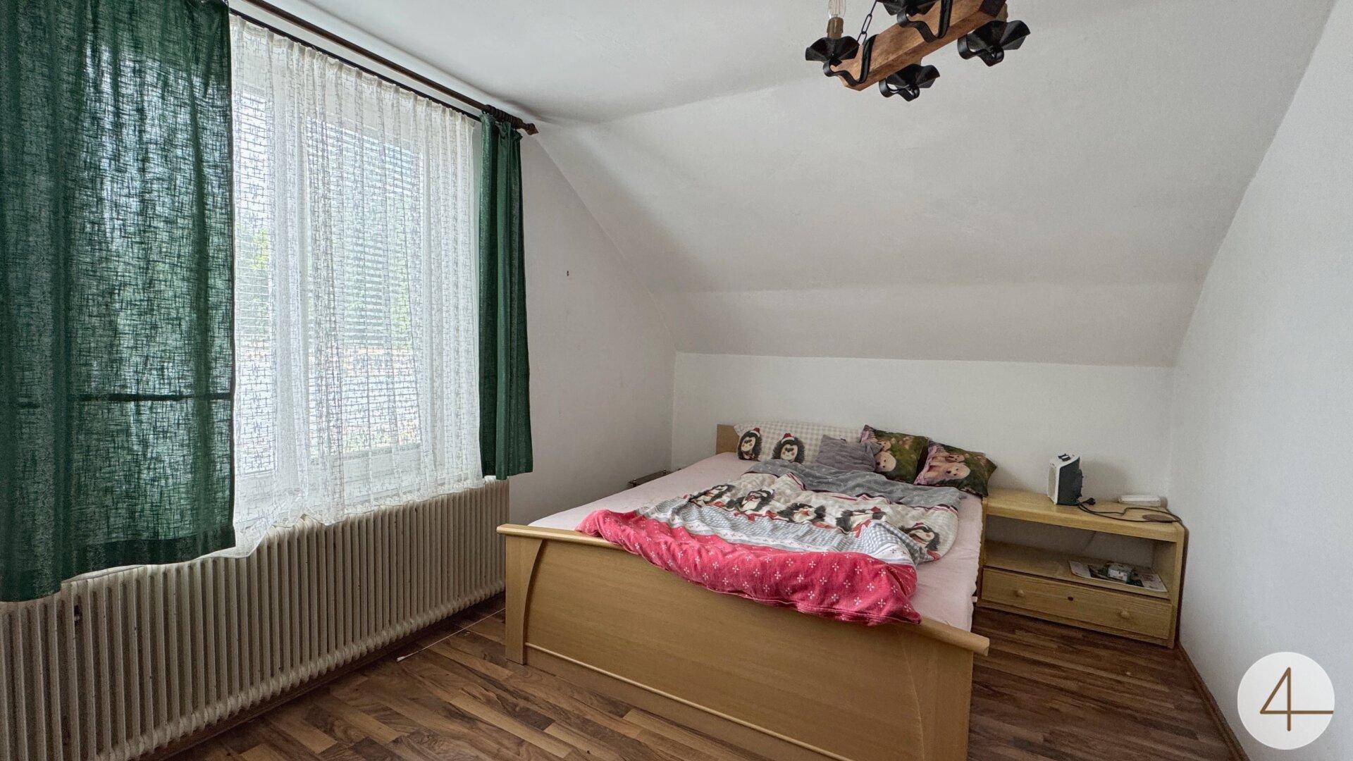 Gemütliches Schlafzimmer im Dachgeschoss mit Schrägdach, Doppelbett und Fenster für angenehmes Tageslicht.