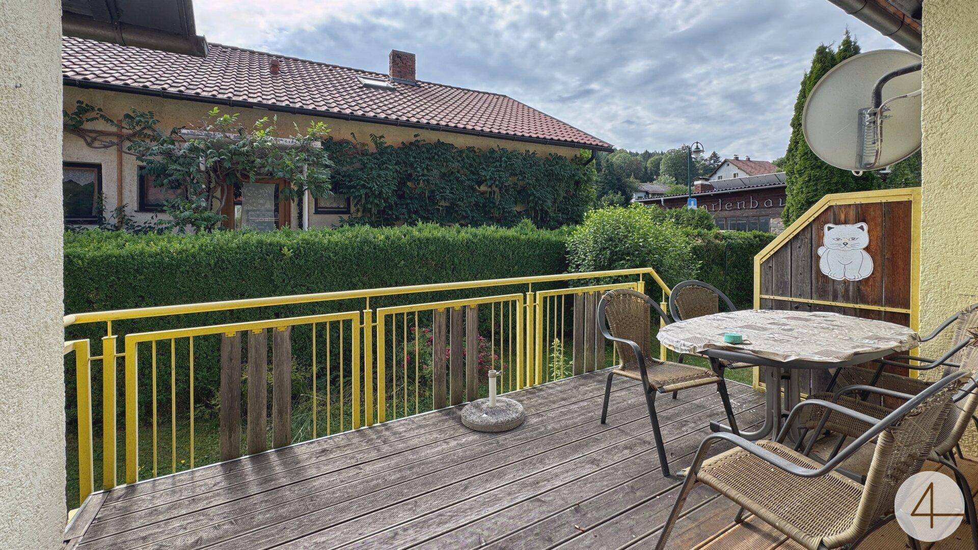 Holzterrasse mit gelbem Geländer und Gartenmöbeln, bietet einen angenehmen Blick ins Grüne.