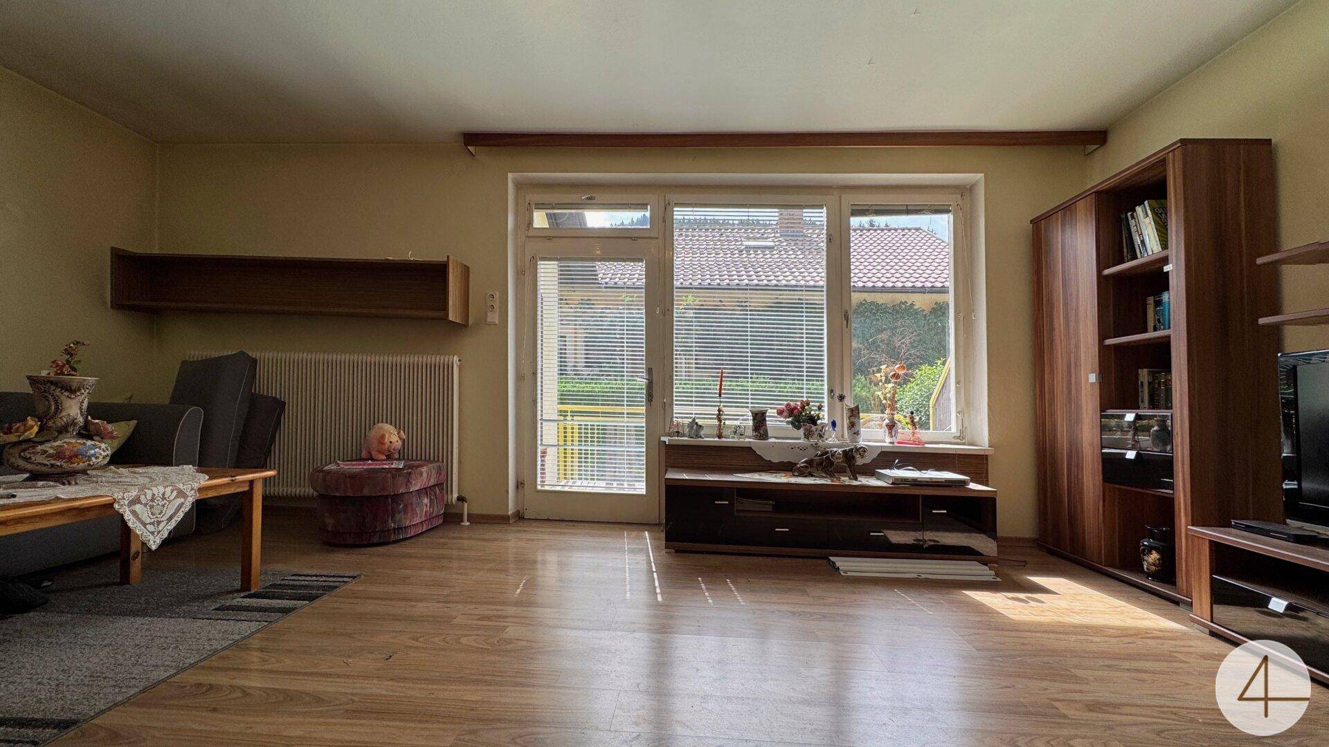 Helles Wohnzimmer mit Laminatboden, bequemer Couch und großem Fenster mit Zugang nach draußen.