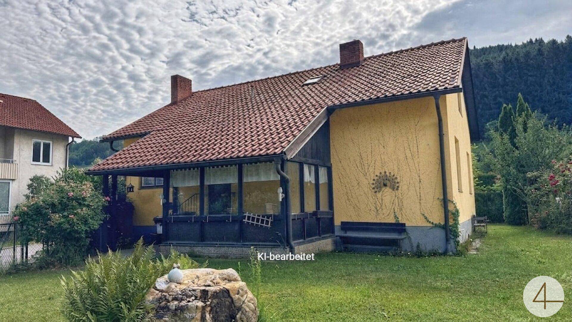 Sonnige Ansicht des Hauses mit einem Wintergarten und einem roten Ziegeldach, umgeben von Grün.
