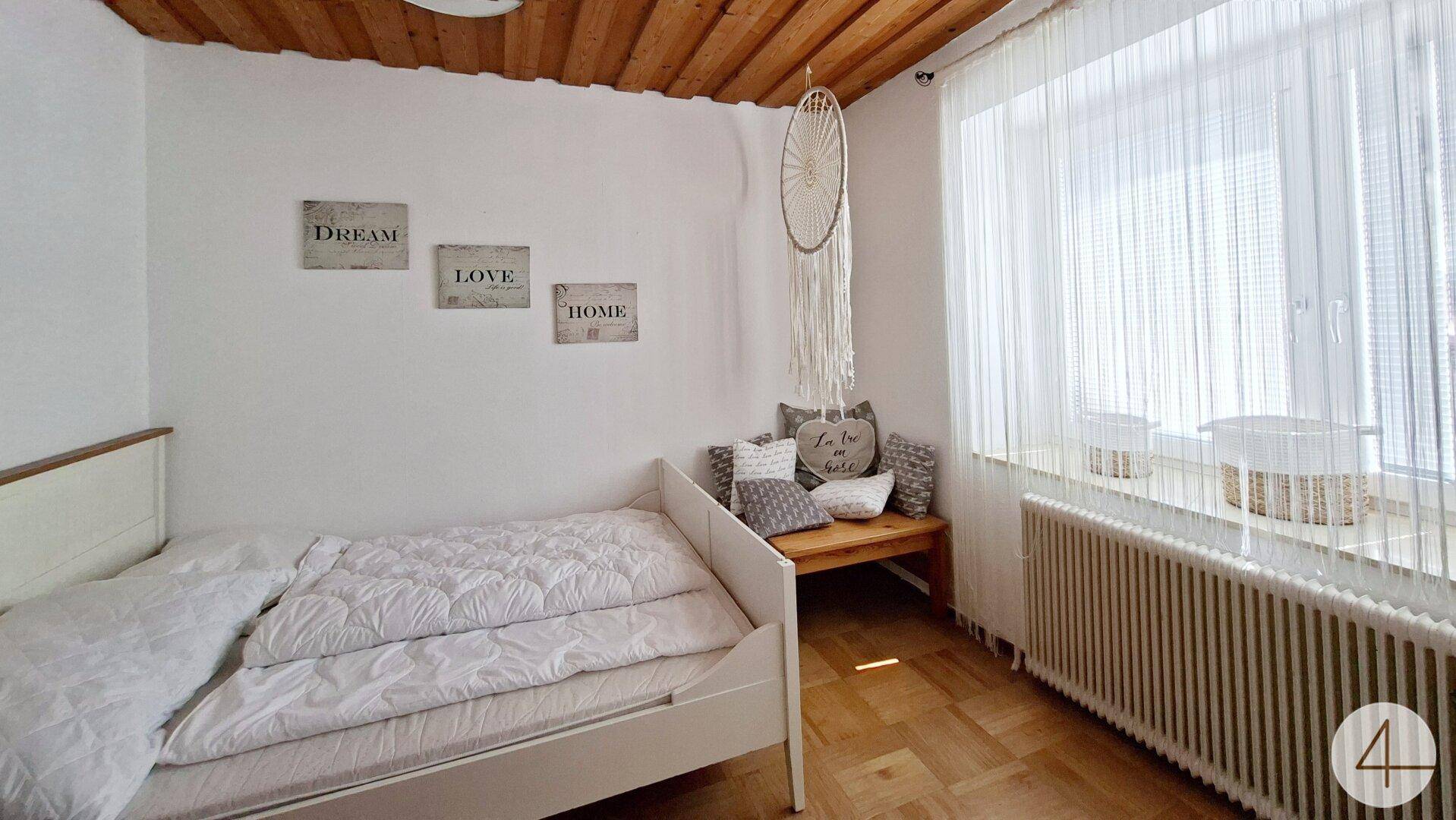 Schlafzimmer mit Einzelbett, Holzboden und dekorativen Wandbildern.