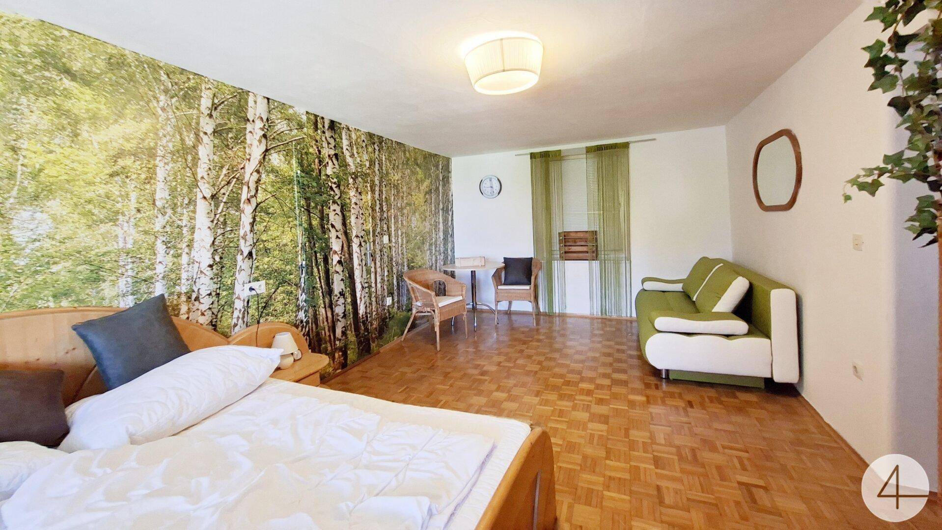 Schlafzimmer mit Holzboden, Wandtapete im Waldmotiv und grünem Sofa.