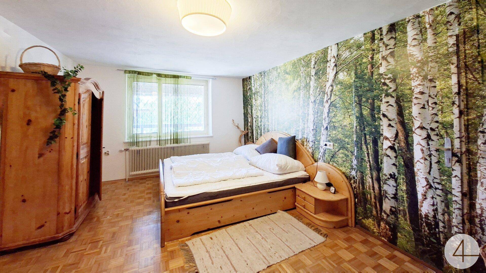 Gemütliches Schlafzimmer mit Doppelbett, Holzschrank und Waldtapete.
