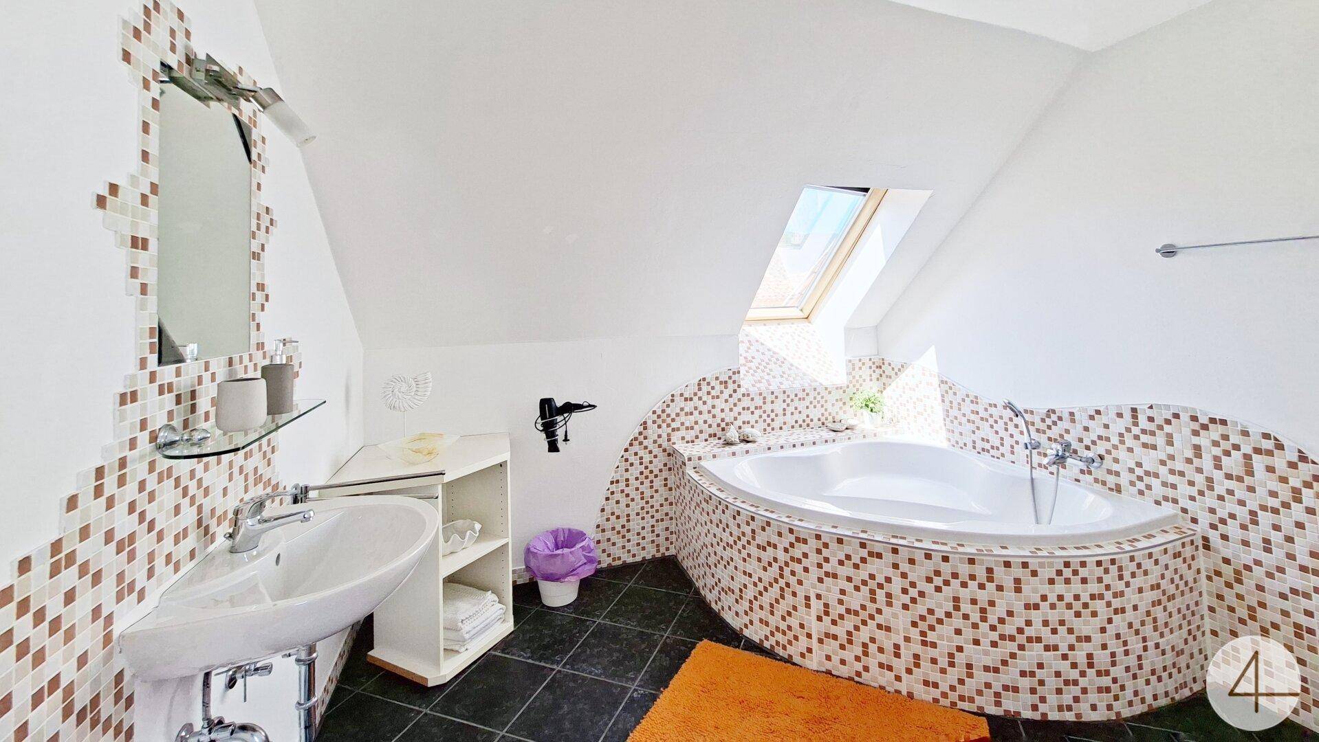 Modernes Badezimmer im Dachgeschoss mit Eckbadewanne, Mosaikfliesen und Dachfenster.