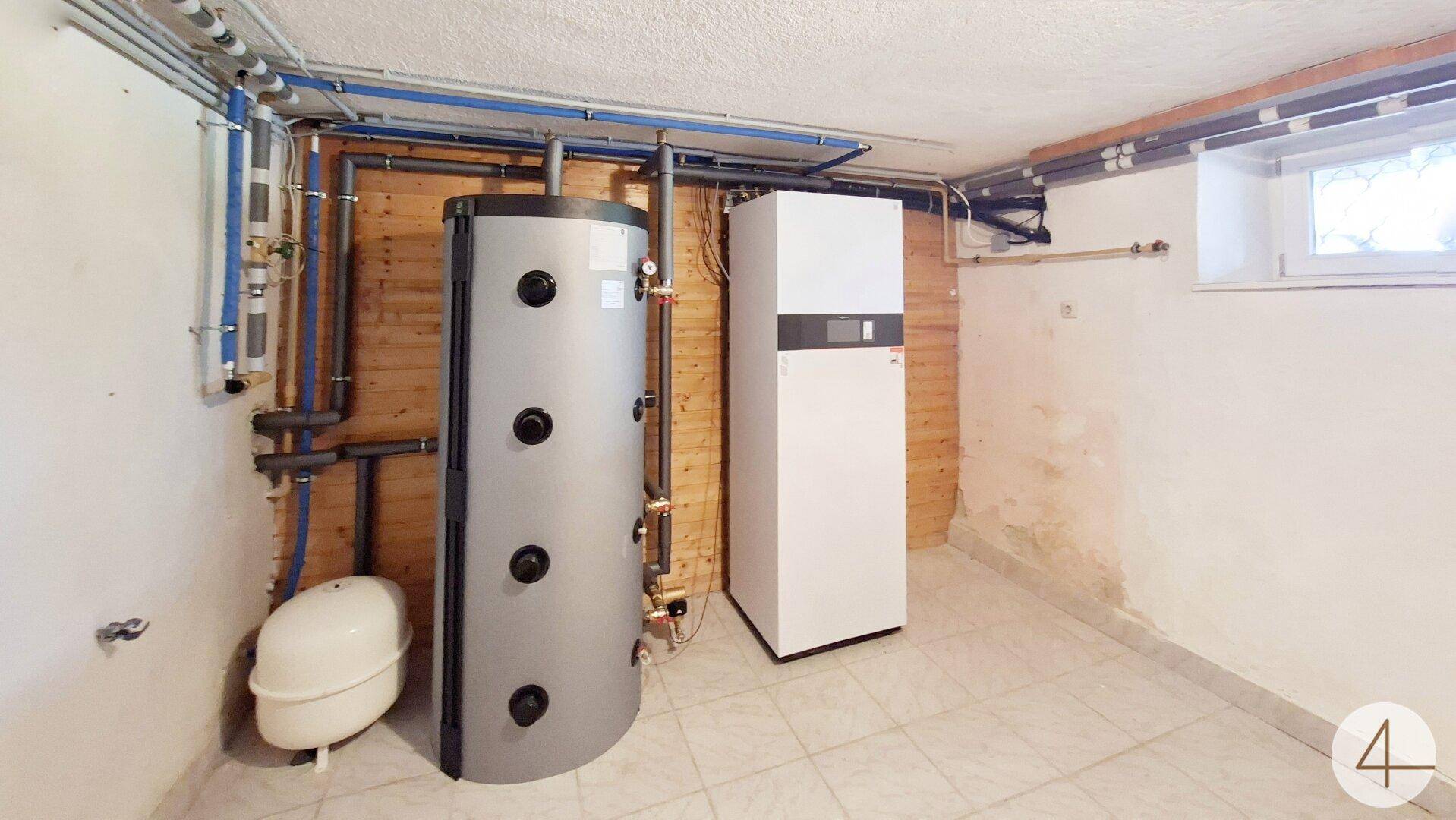 Technikraum im Keller mit moderner Heizungsanlage, Warmwasserspeicher und sichtbaren Leitungen.