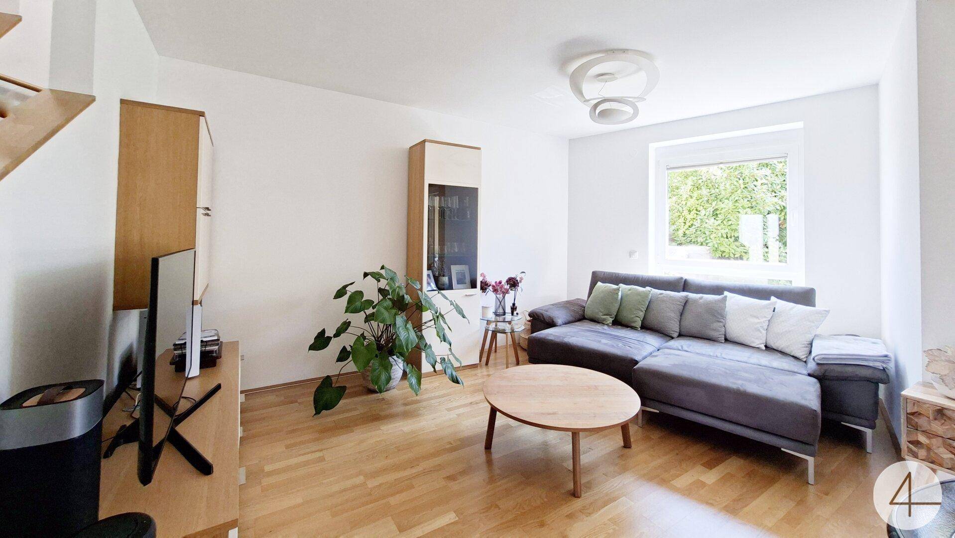Heller Wohnbereich mit großem Sofa, Holzboden und Blick ins Grüne.