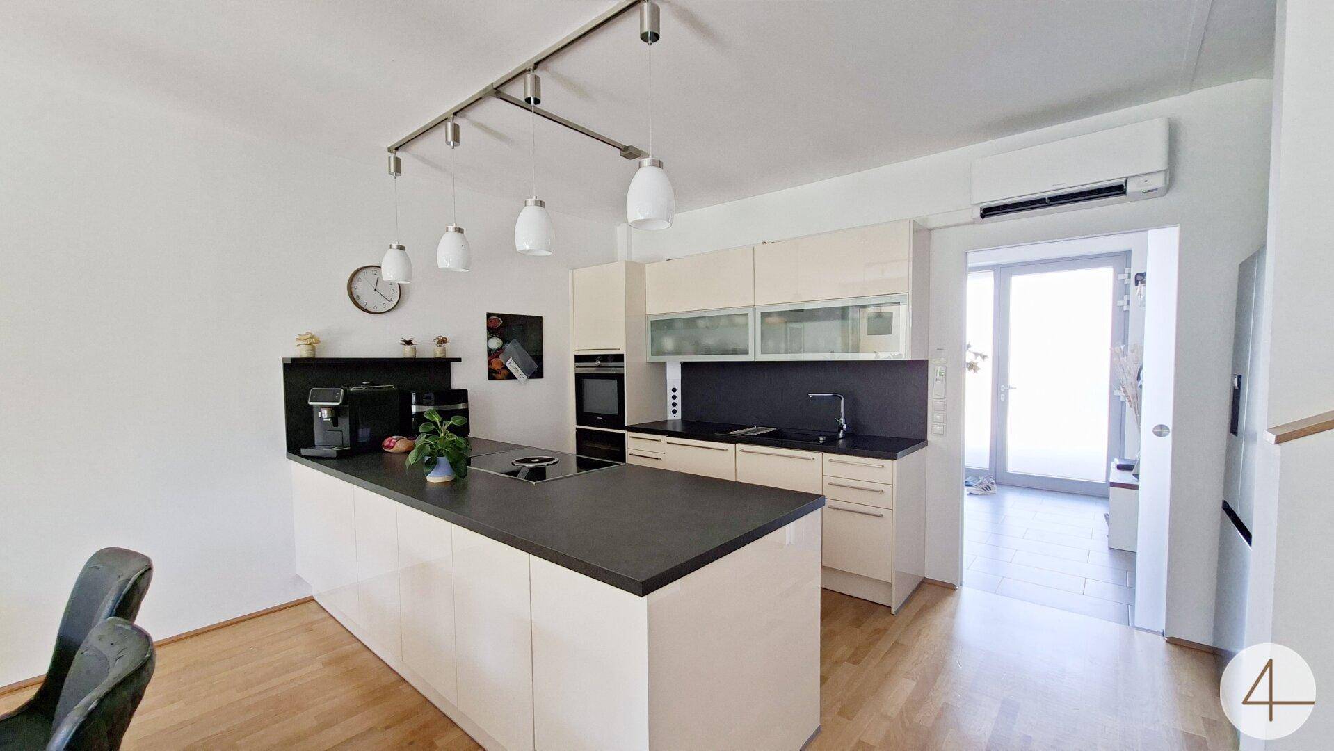 Moderne Küche mit Kücheninsel, dunkler Arbeitsplatte und integrierten Geräten.