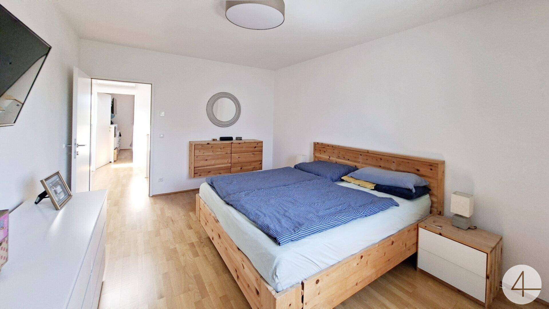 Schlafzimmer mit Doppelbett, Holzboden und schlichter Einrichtung.