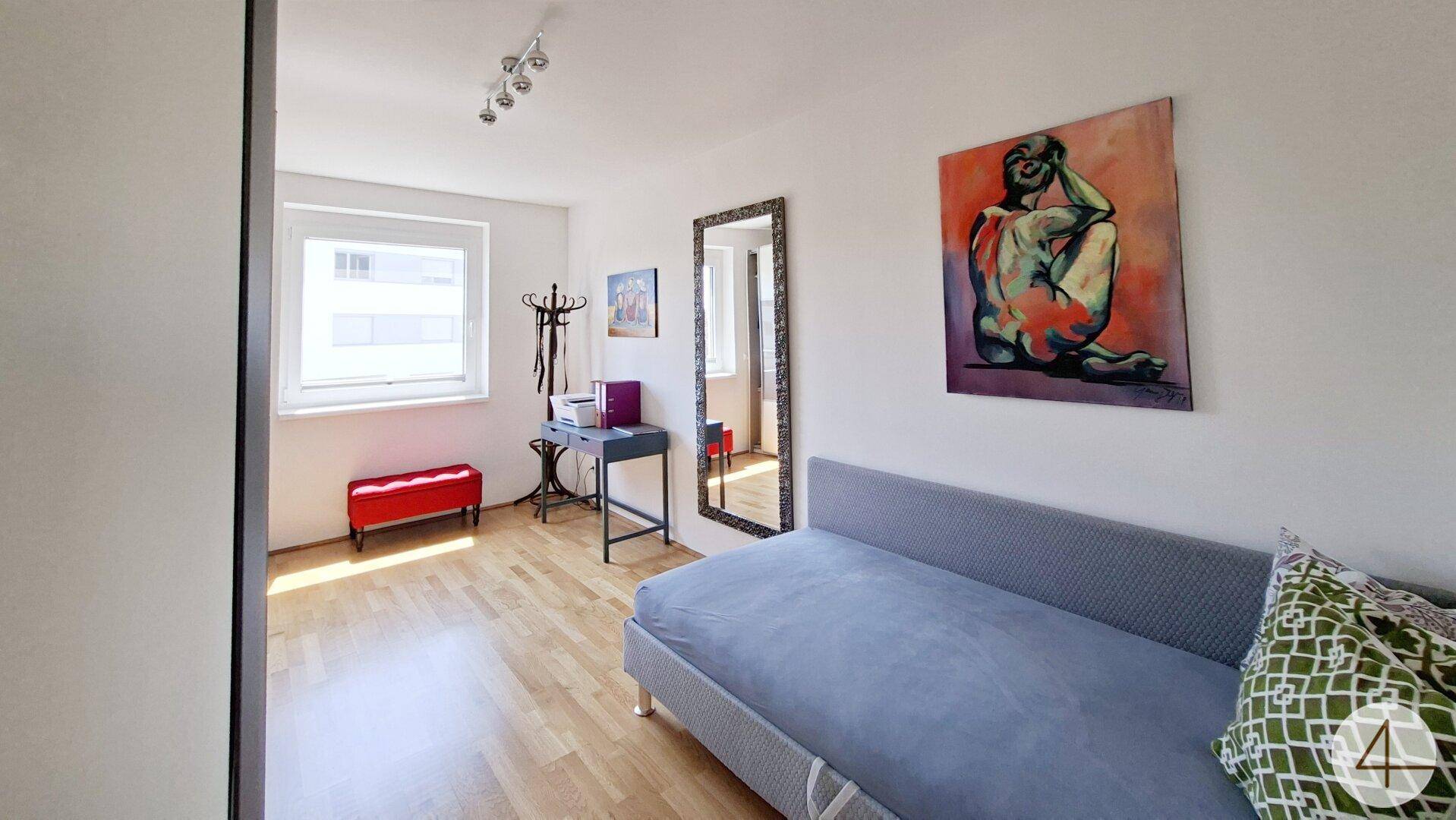Helles Zimmer mit Schlafsofa, Holzboden und großem Spiegel.