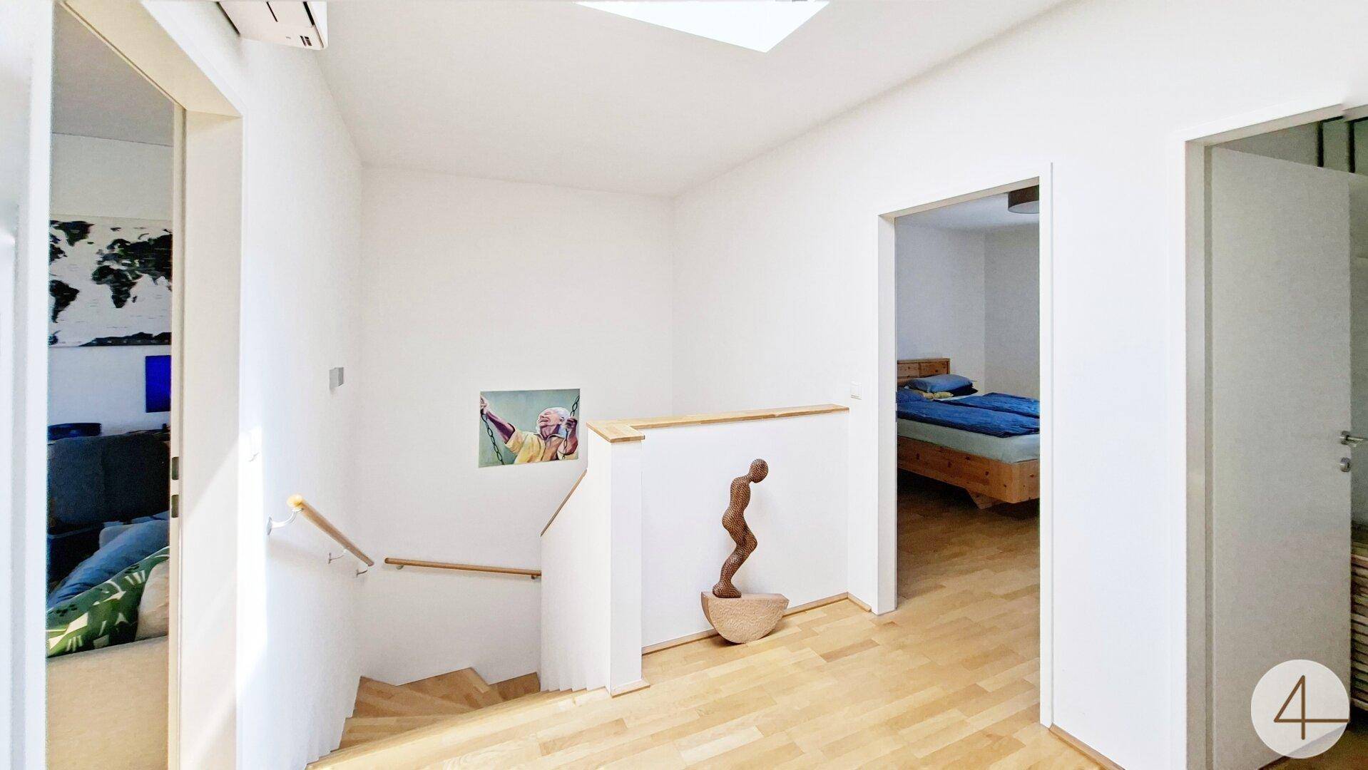 Heller Flur im Obergeschoss mit Treppenabgang und Holzboden.