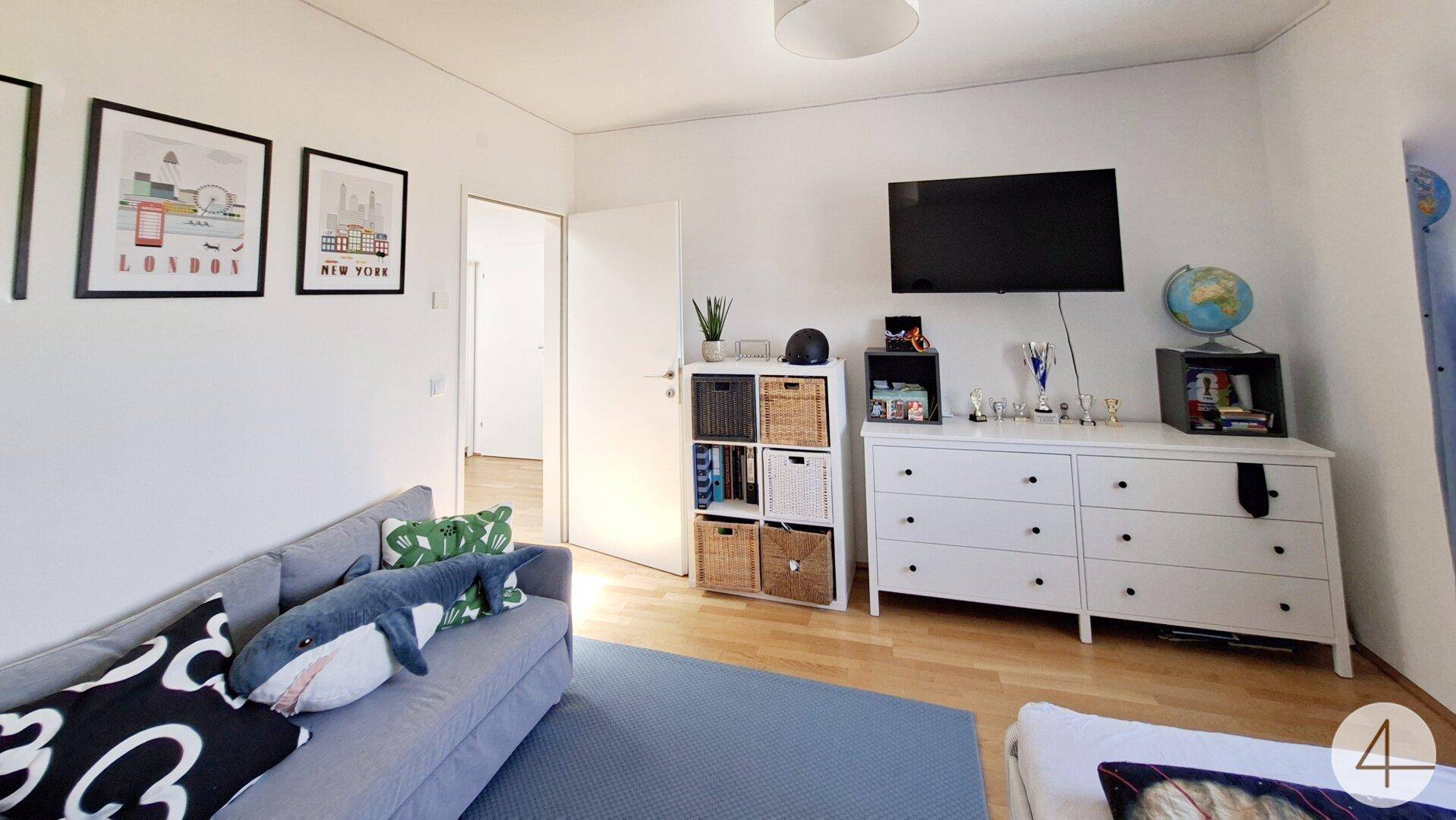 Kinderzimmer mit Sofa, Kommode und Wanddekoration.