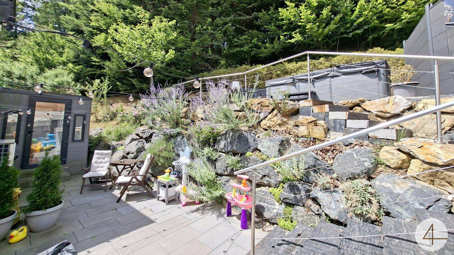 Gemütliche Terrasse mit Sitzgelegenheiten und einem Whirlpool, umgeben von Felsen und Pflanzen.